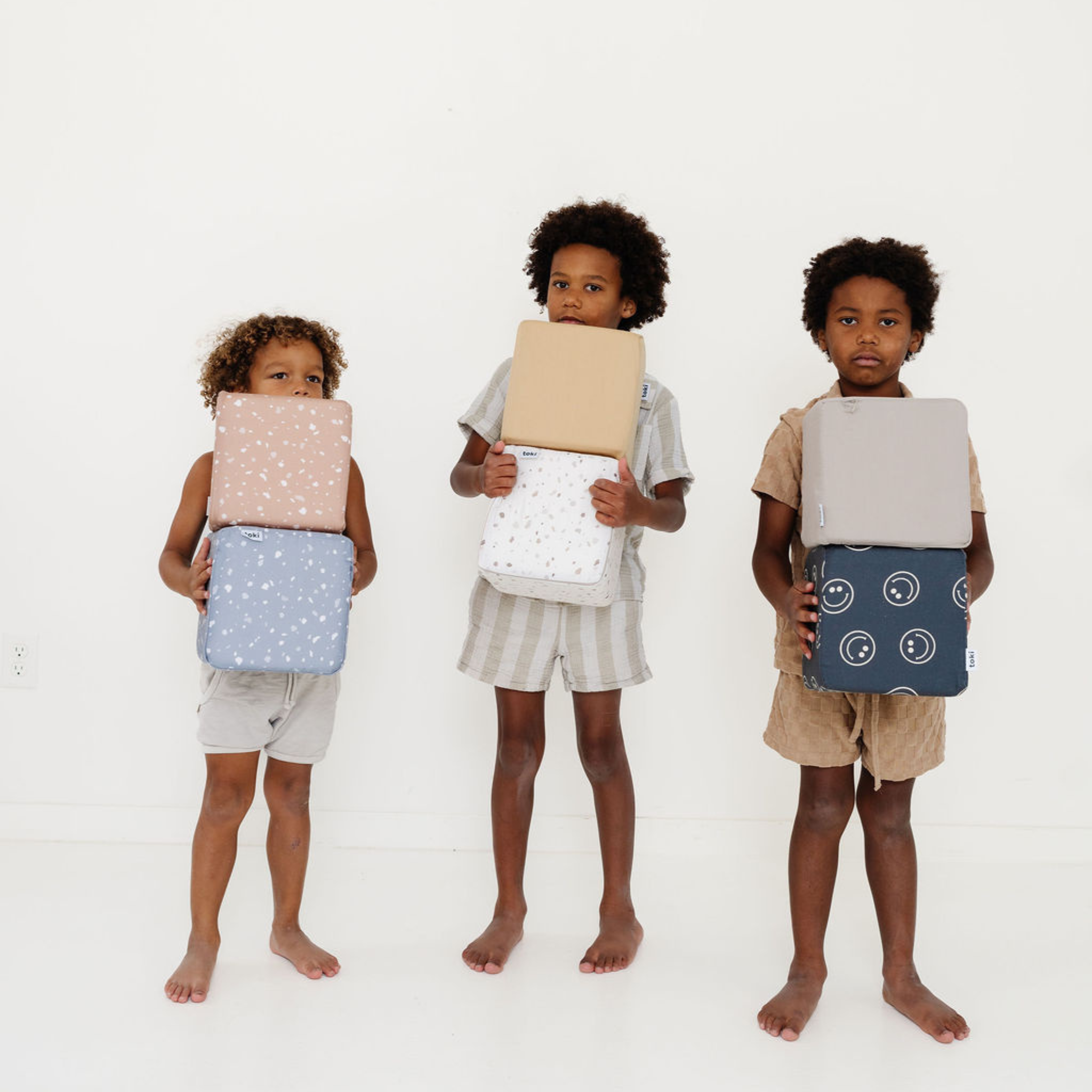 Three children holding colorful bags against a white background