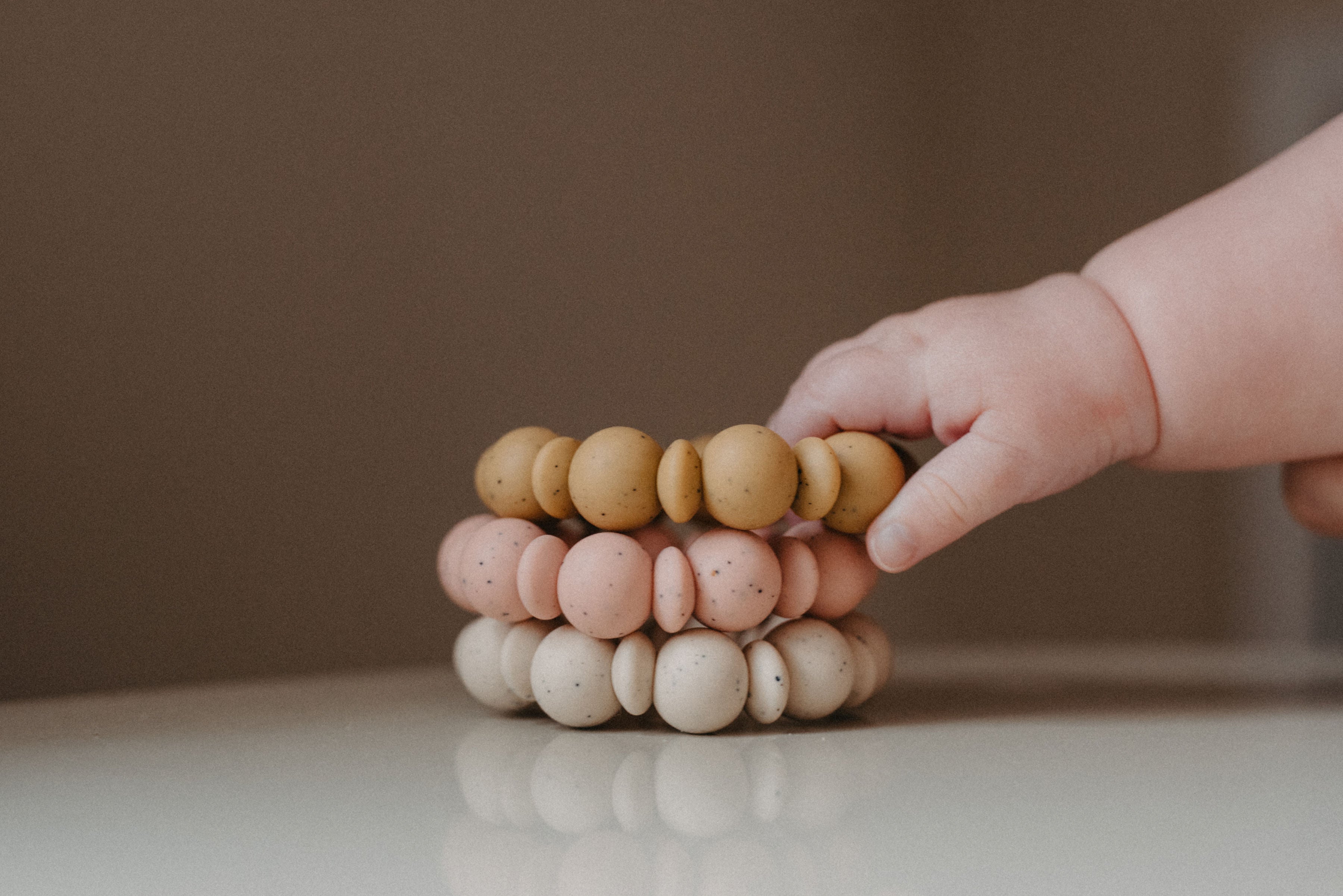 Stack of wooden beads with a child's hand reaching towards them on a neutral background