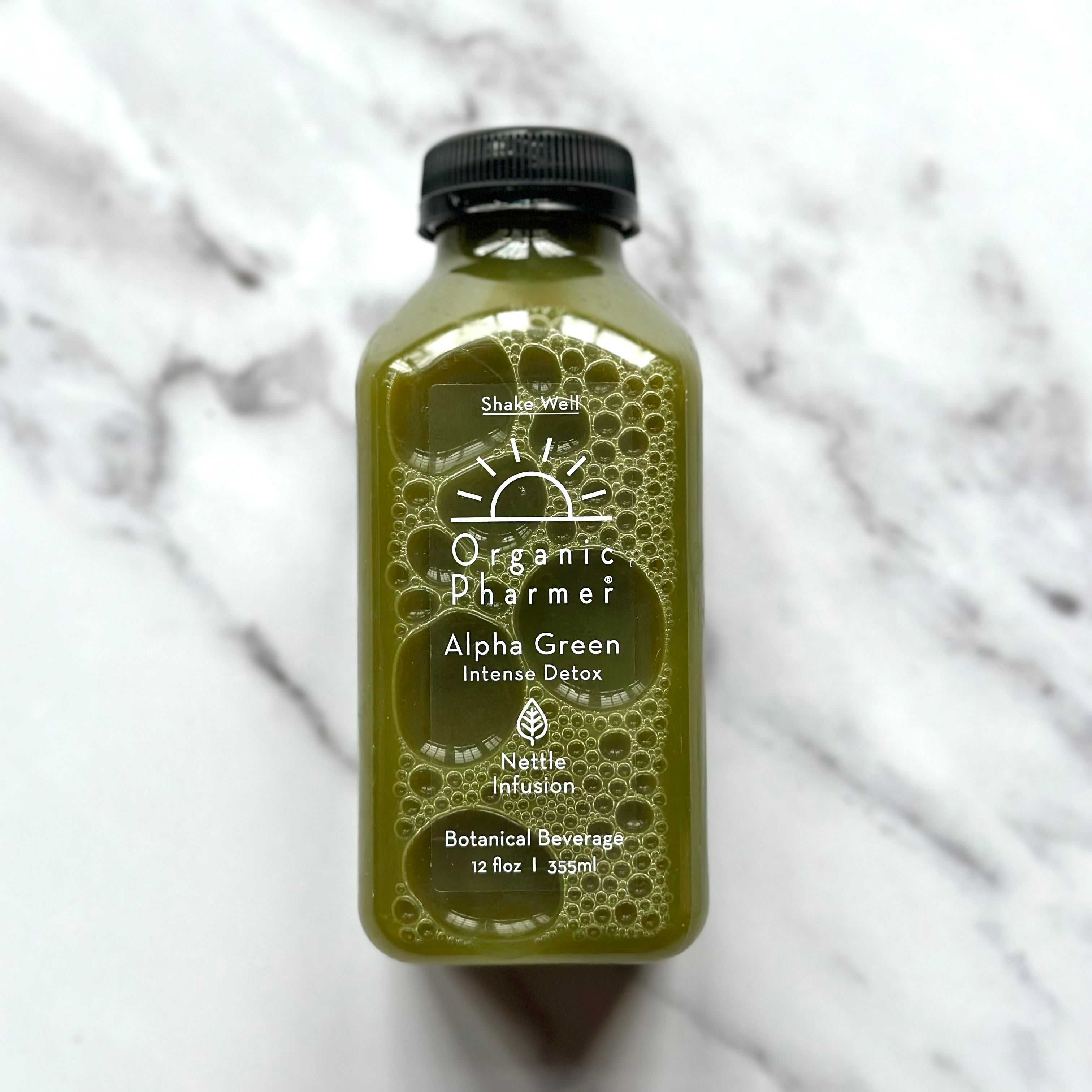 Bottle of Organic Pharmer Alpha Green Intense Detox beverage on a marble surface