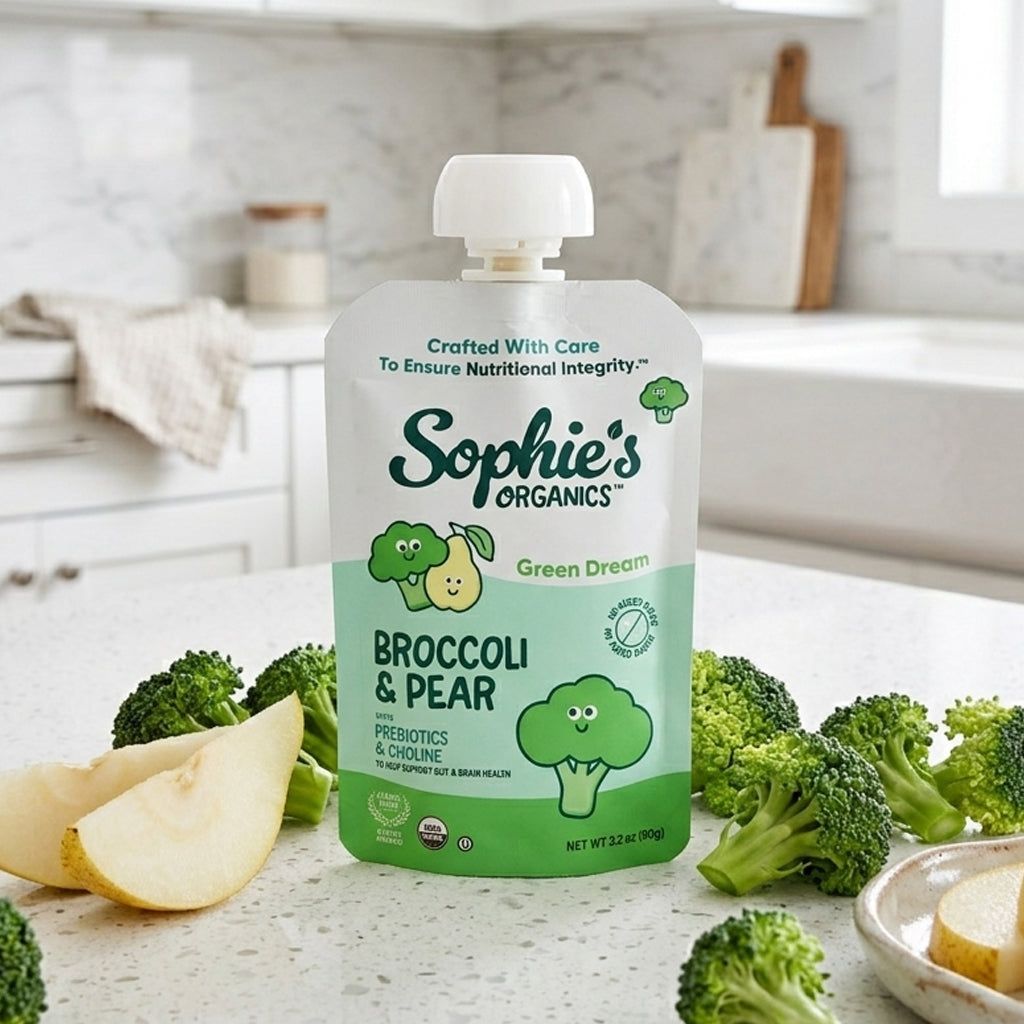 Sophie's Organics broccoli and pear baby food pouch on a kitchen counter with broccoli and apple slices.