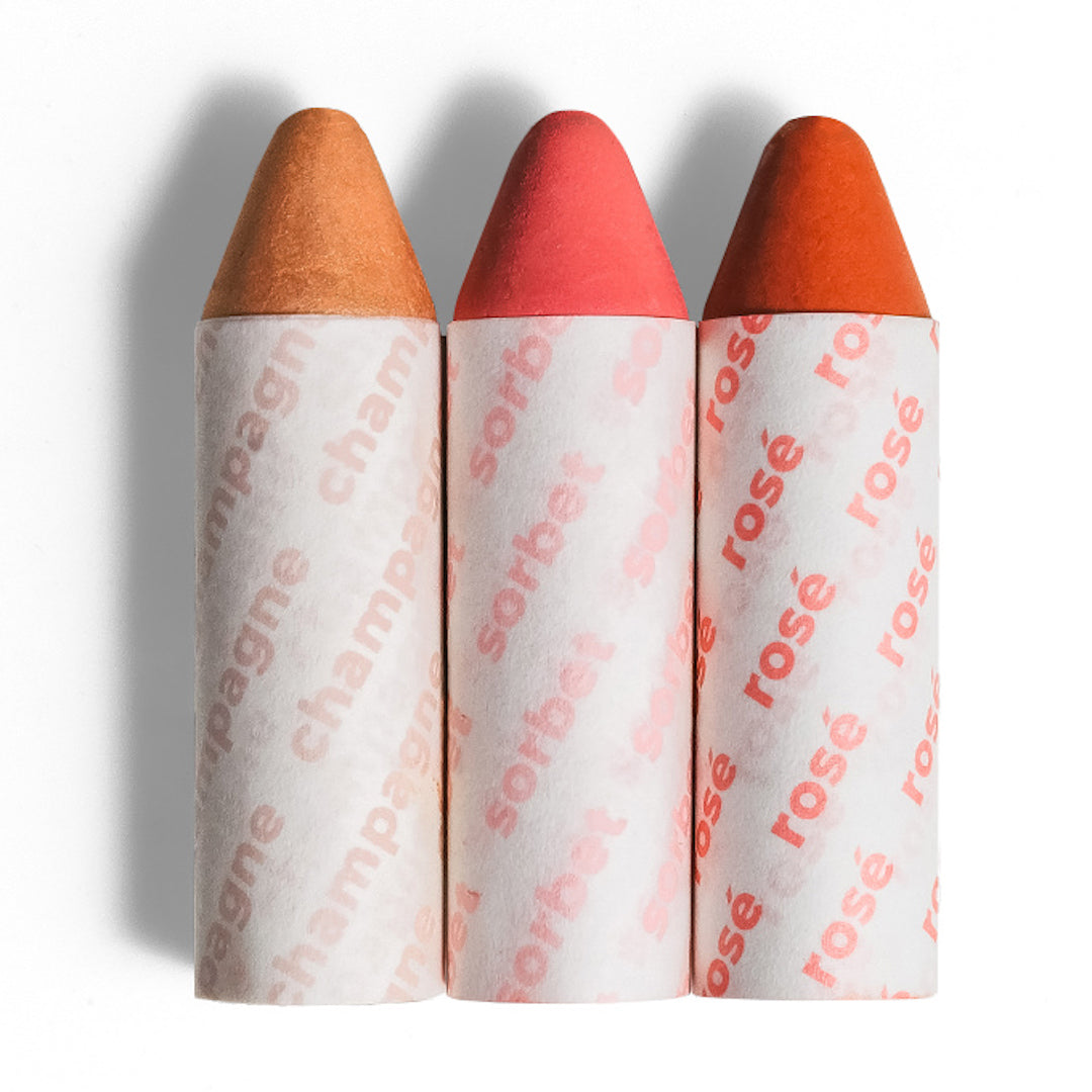 Three cosmetic products with colored caps and branded paper wrappers on a white background
