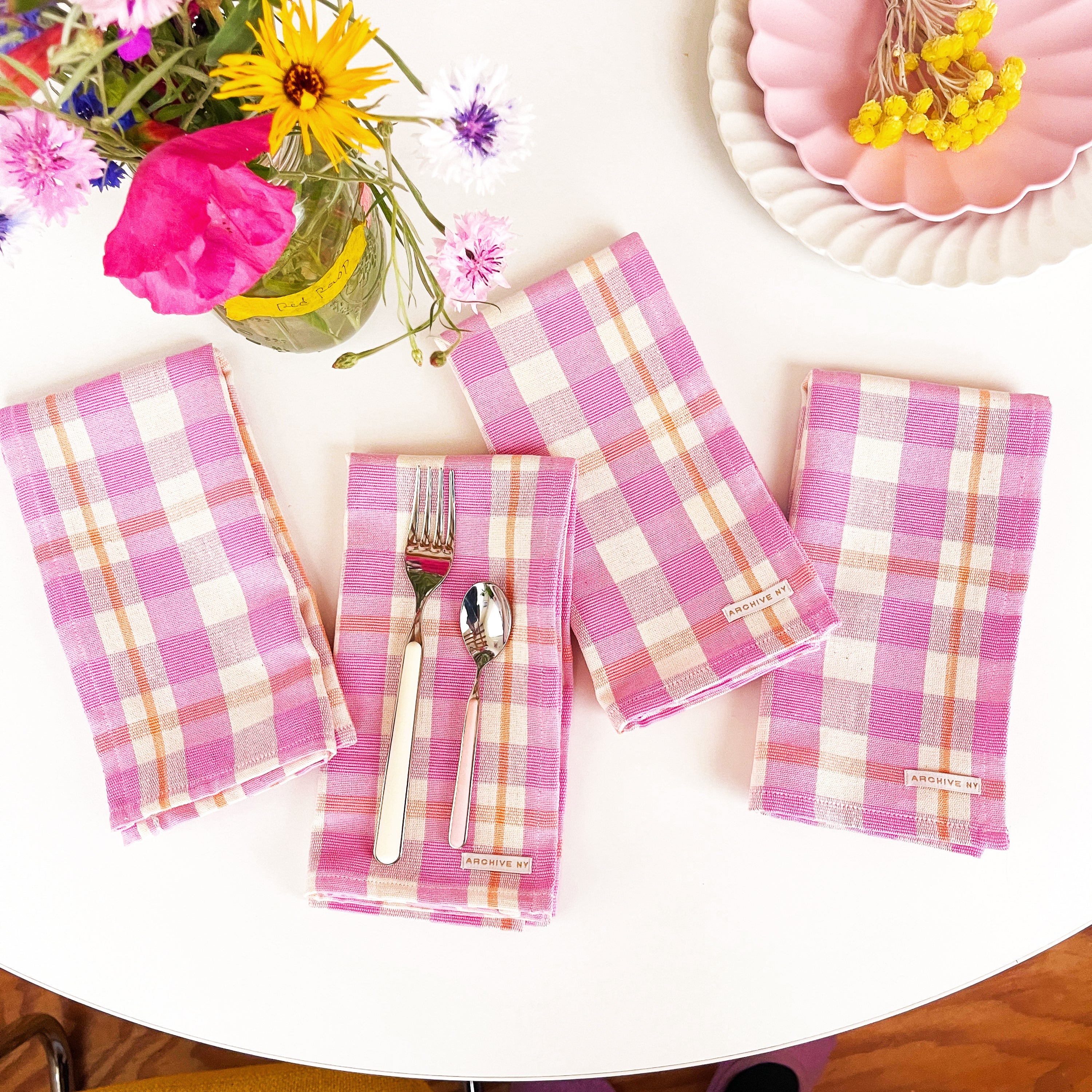 Pink checkered napkins on a table with silverware and flowers.