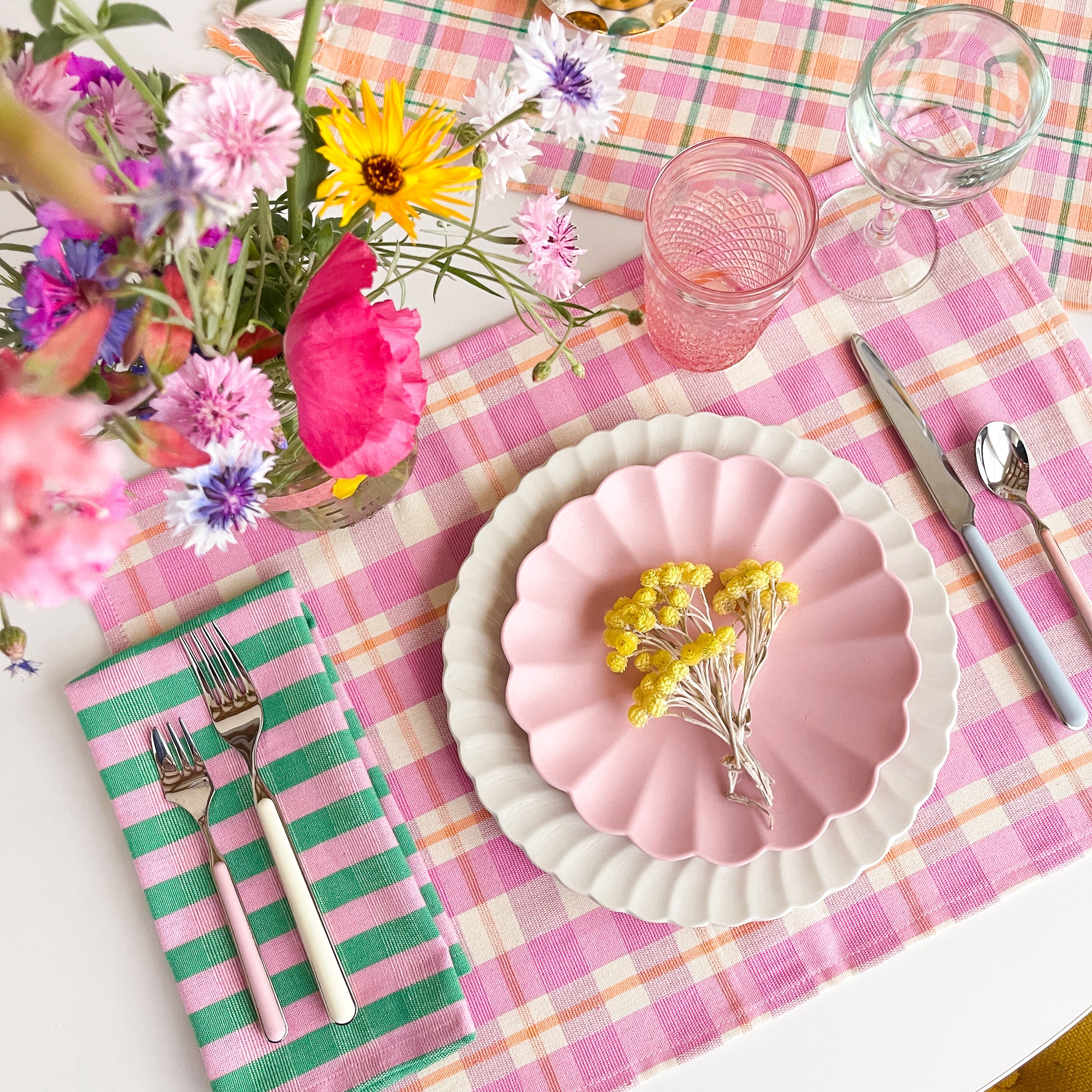 Table setting with pink plates, flowers, and cutlery on a checkered tablecloth.