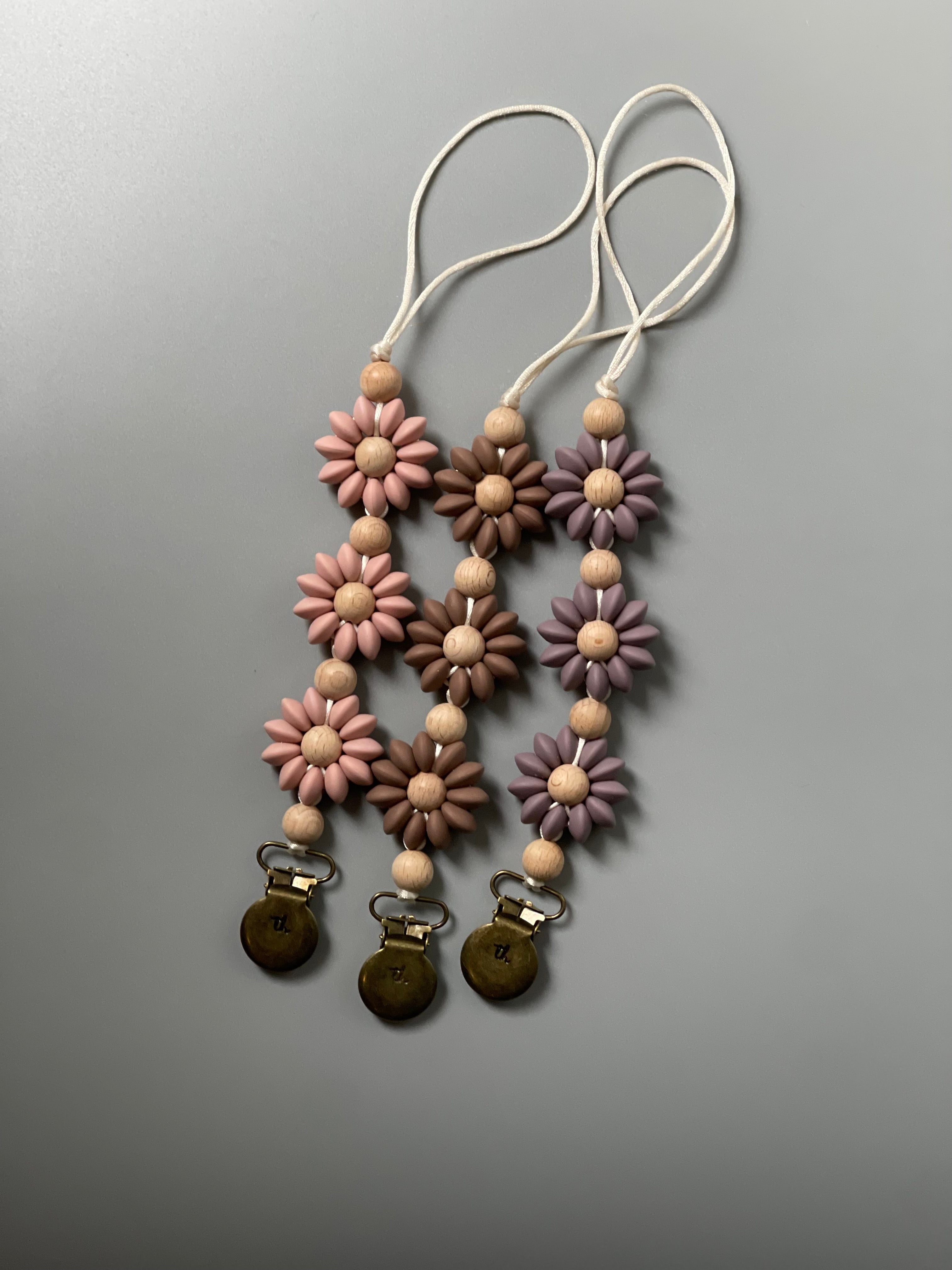 Flower-shaped pacifier clips with wooden beads on a gray background