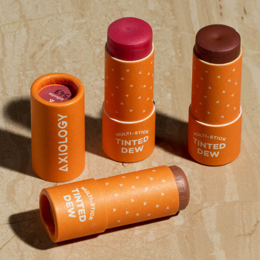 Multiple orange Axiology multi-stick tinted deodorants on a beige background