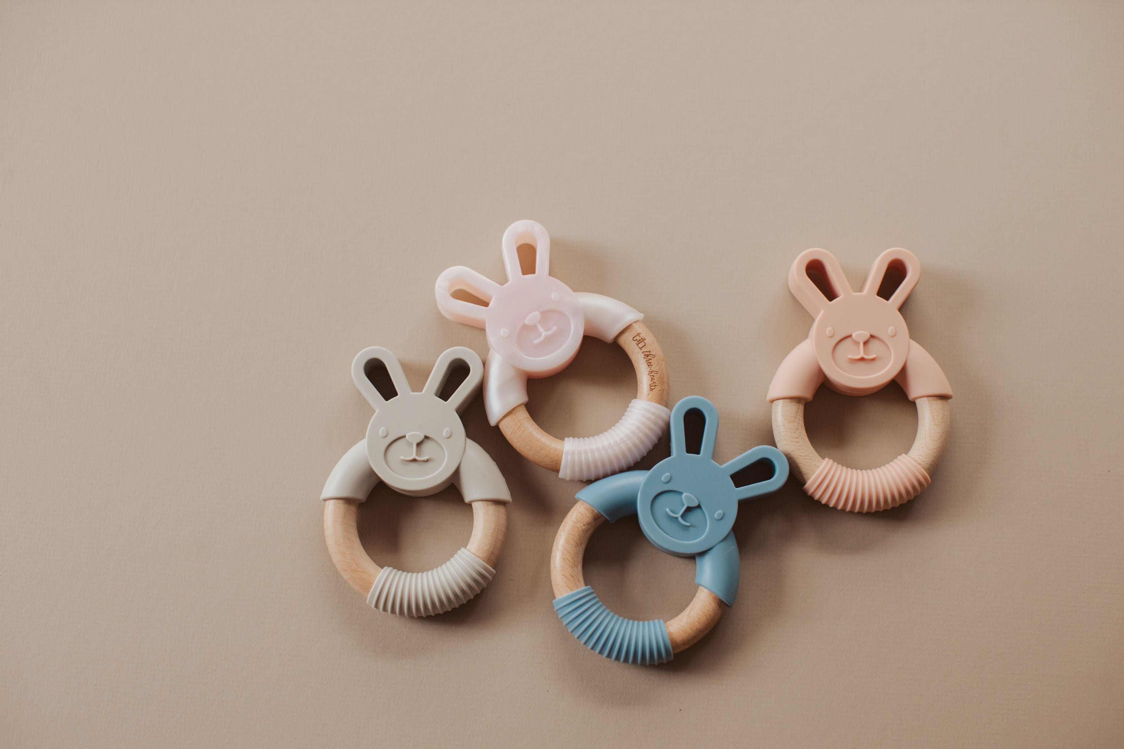Four bunny-shaped teething rings in different colors on a beige background