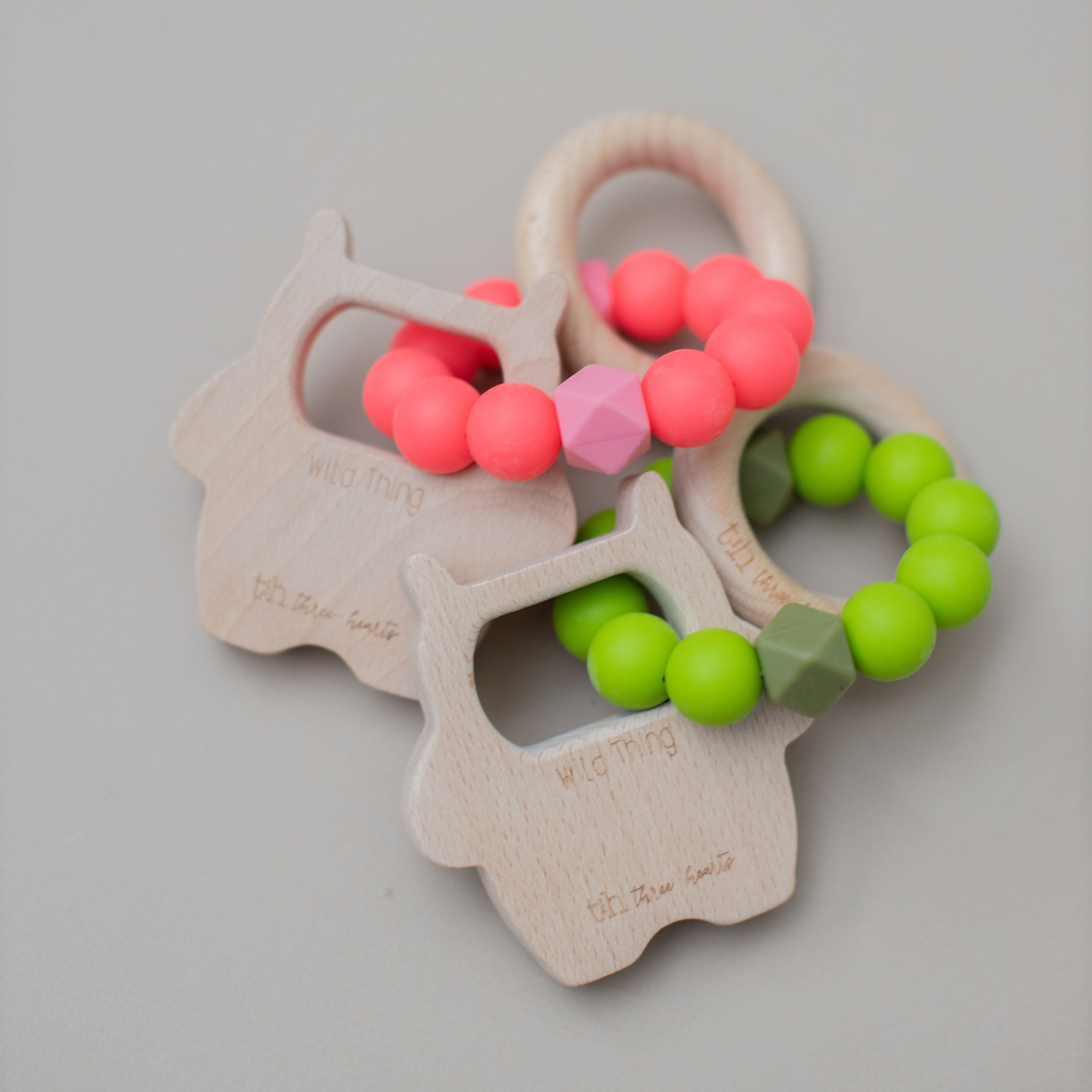 Two baby teething toys with pink and green beads on a gray background