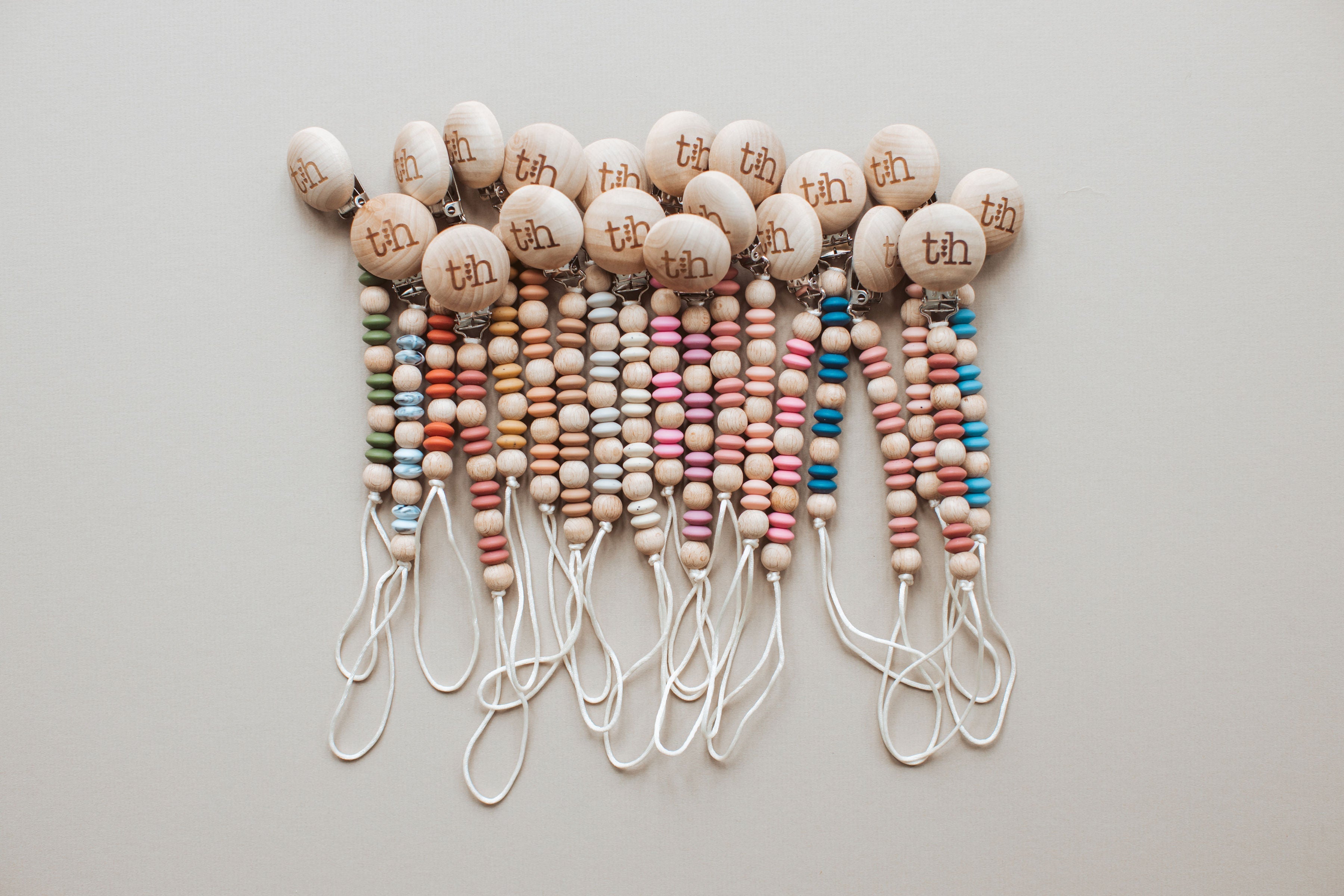 Collection of colorful beaded lanyards with 'tbh' tags on a light gray background