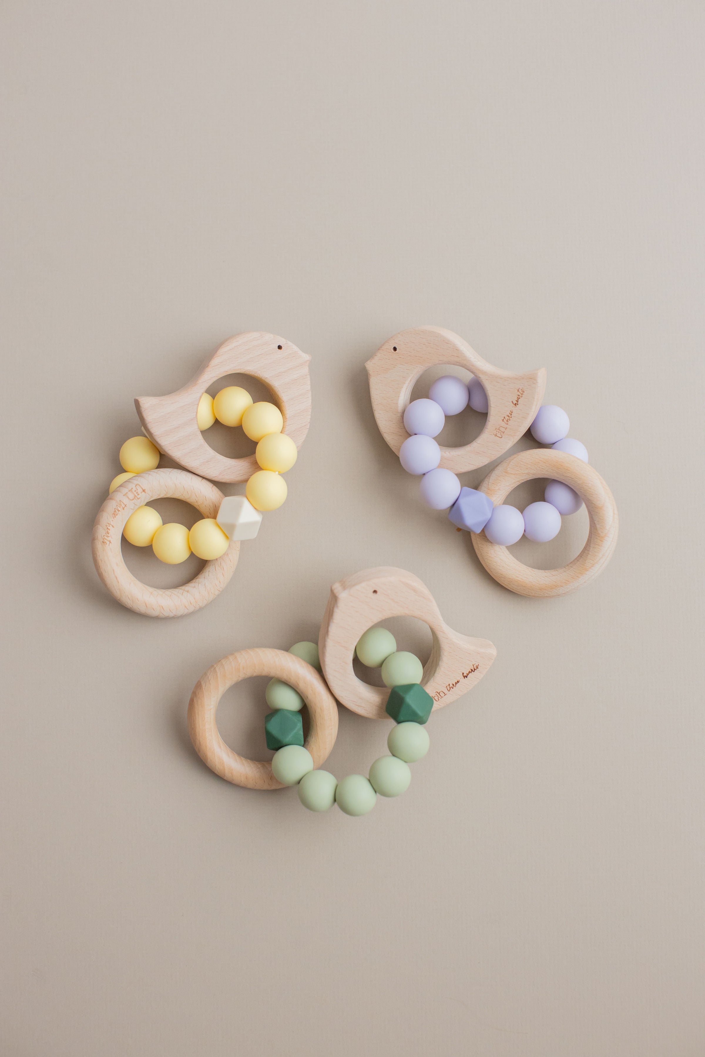 Three wooden teething rings with colorful beads on a beige background