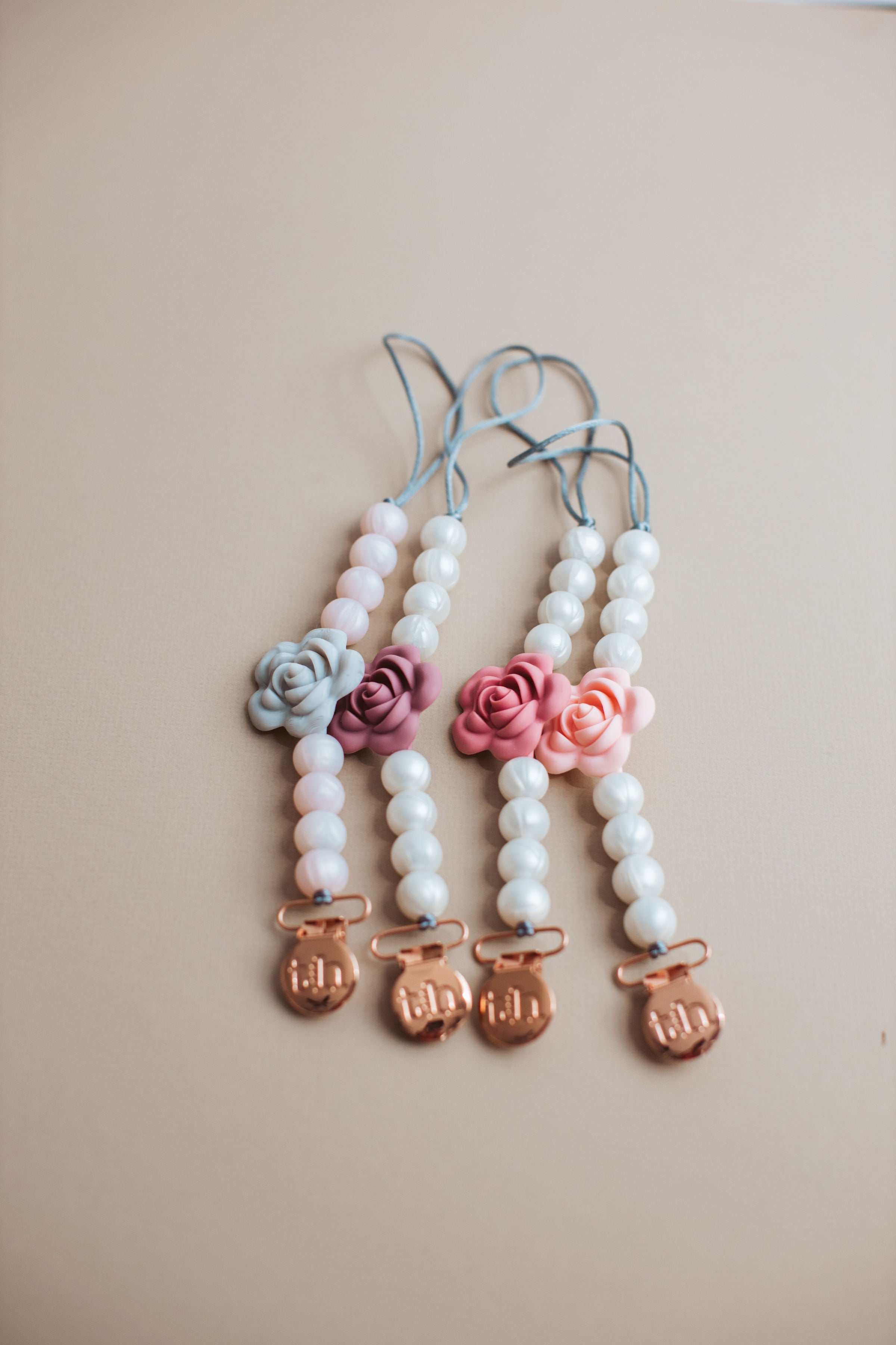 Three baby teether charms with floral designs and initials on a beige background