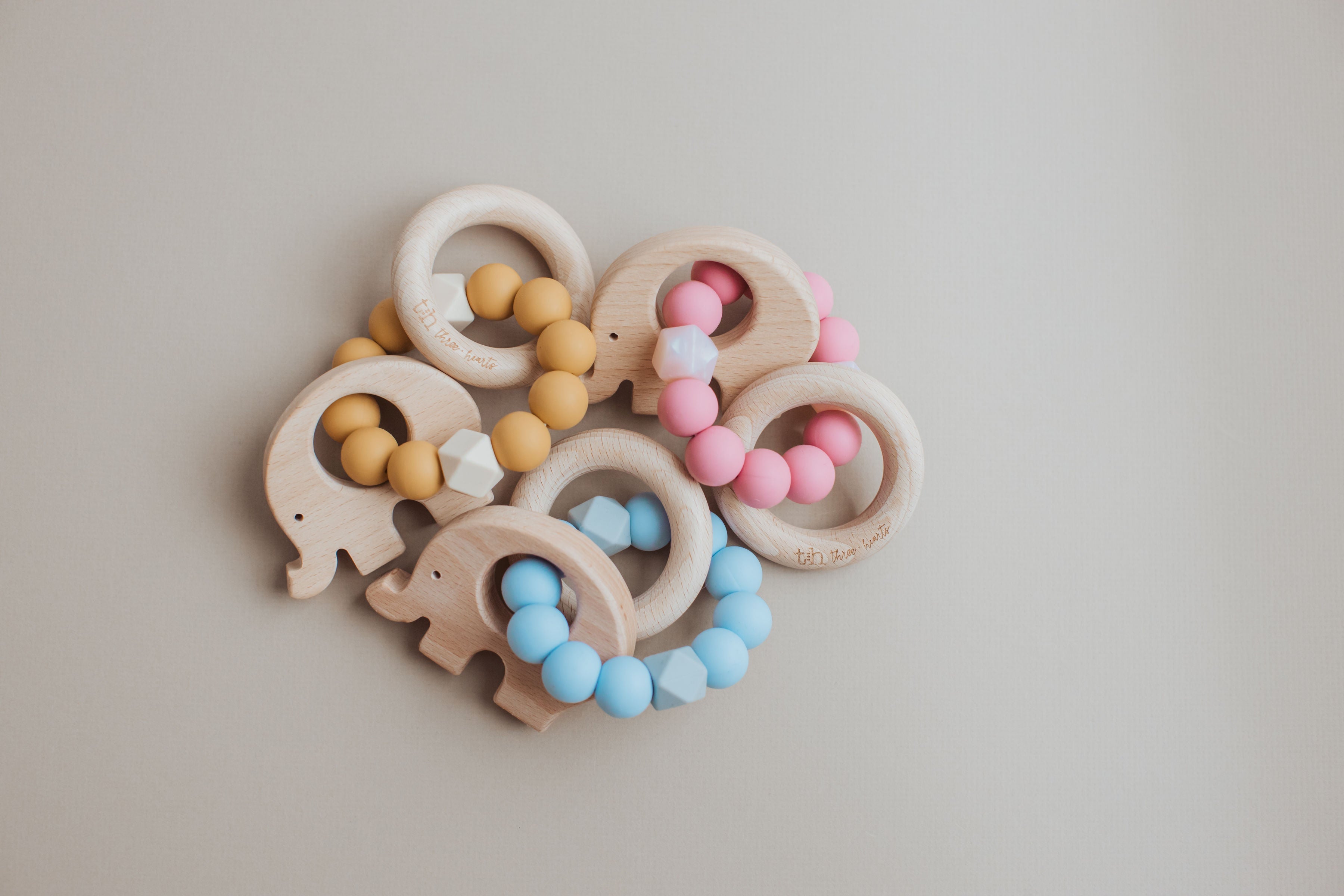 Set of wooden elephant-shaped teething rings with colorful beads on a light gray background
