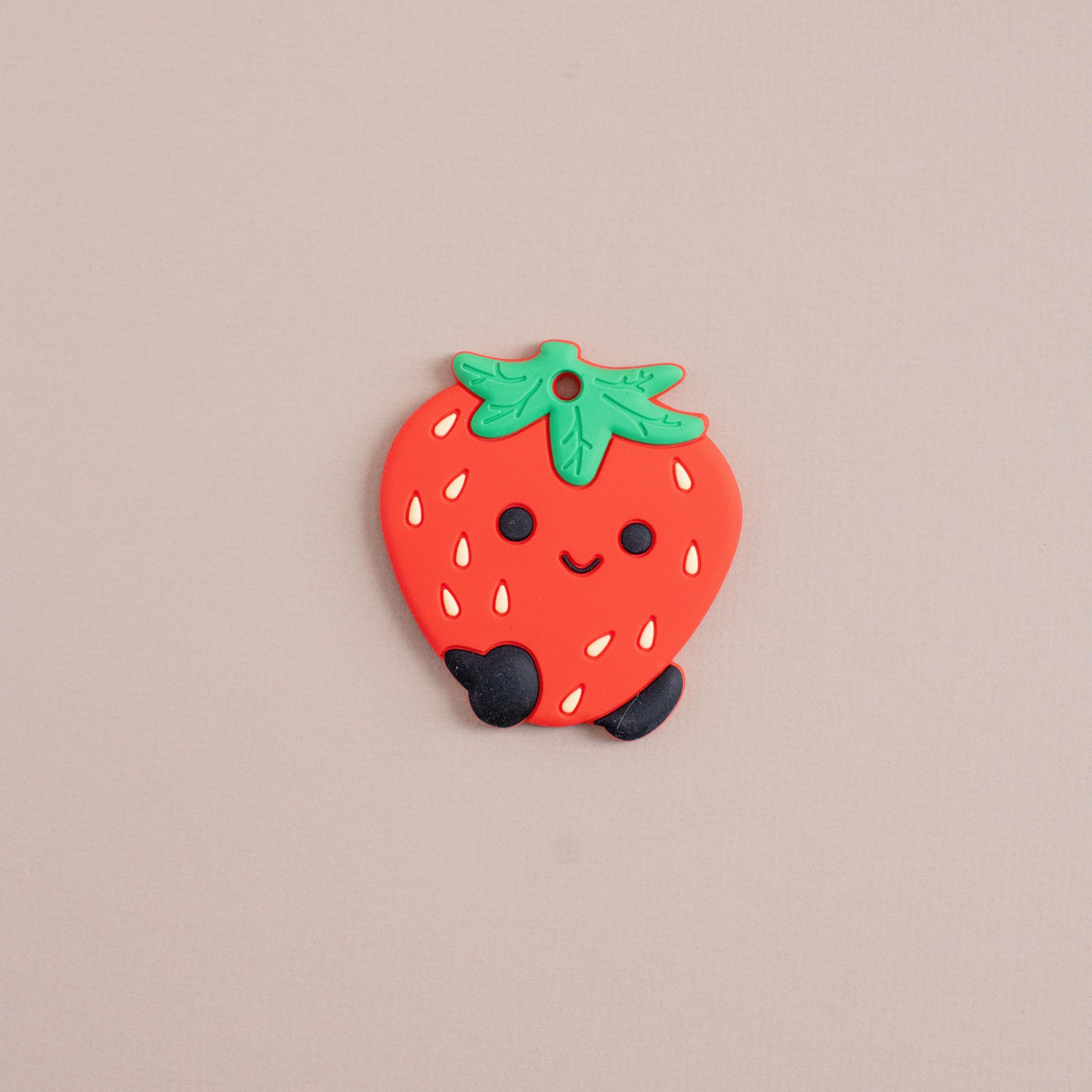Strawberry-shaped charm with a smiling face on a beige background