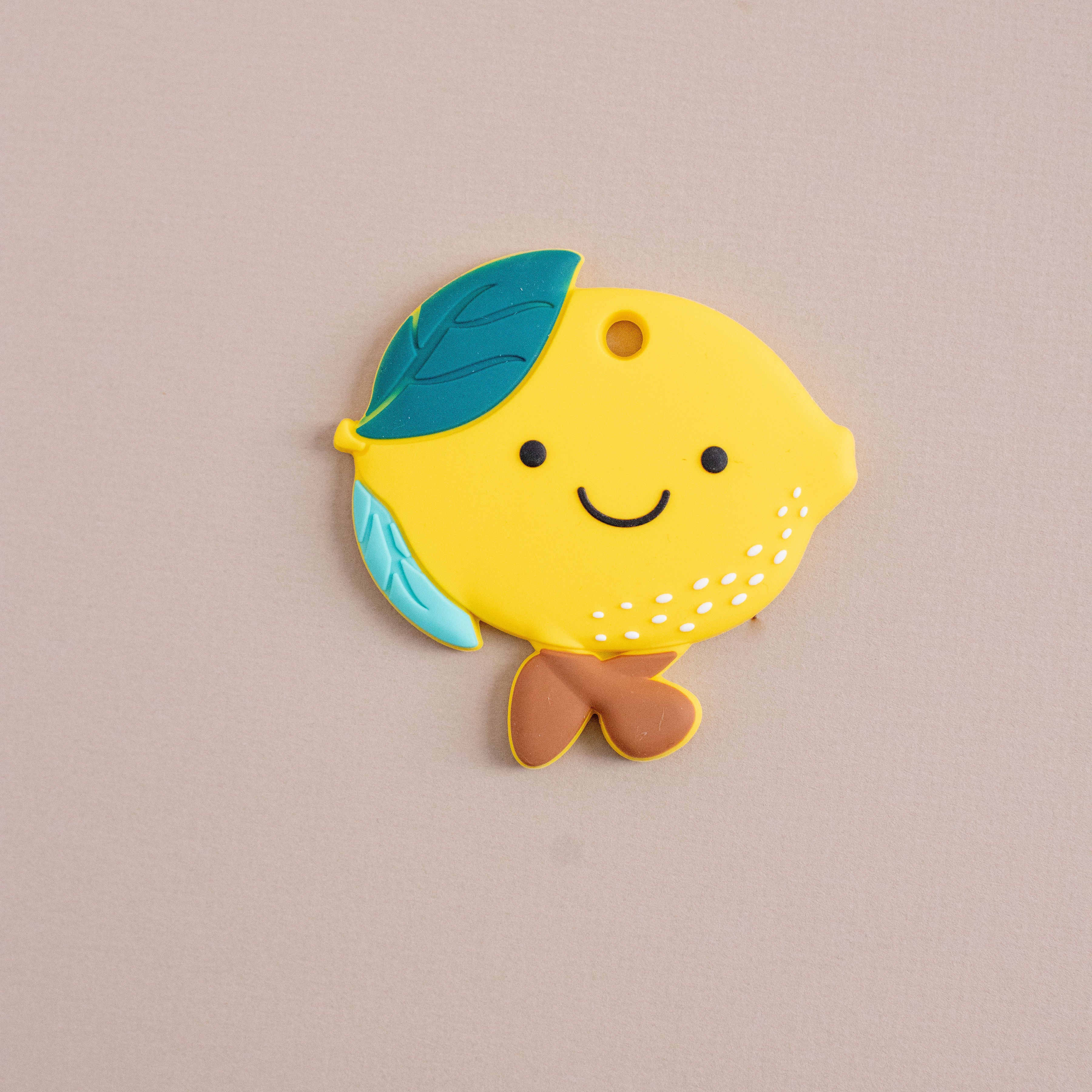 Yellow lemon-shaped keychain with a blue leaf on a beige background