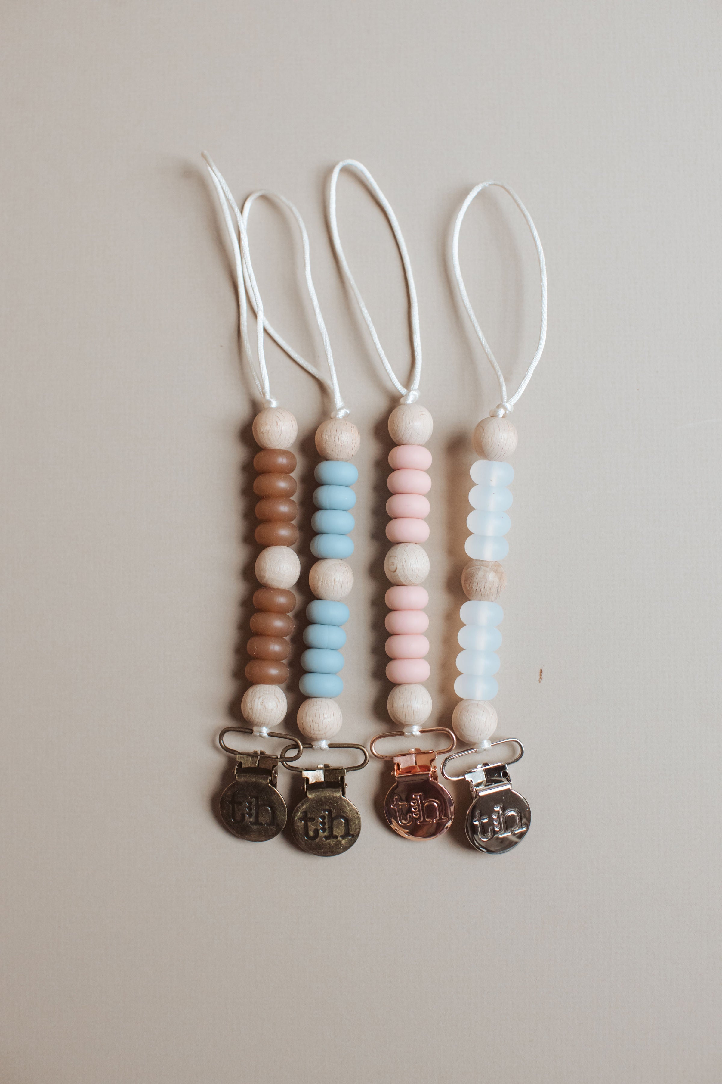 Three baby teething necklaces with beads and charms on a light gray background
