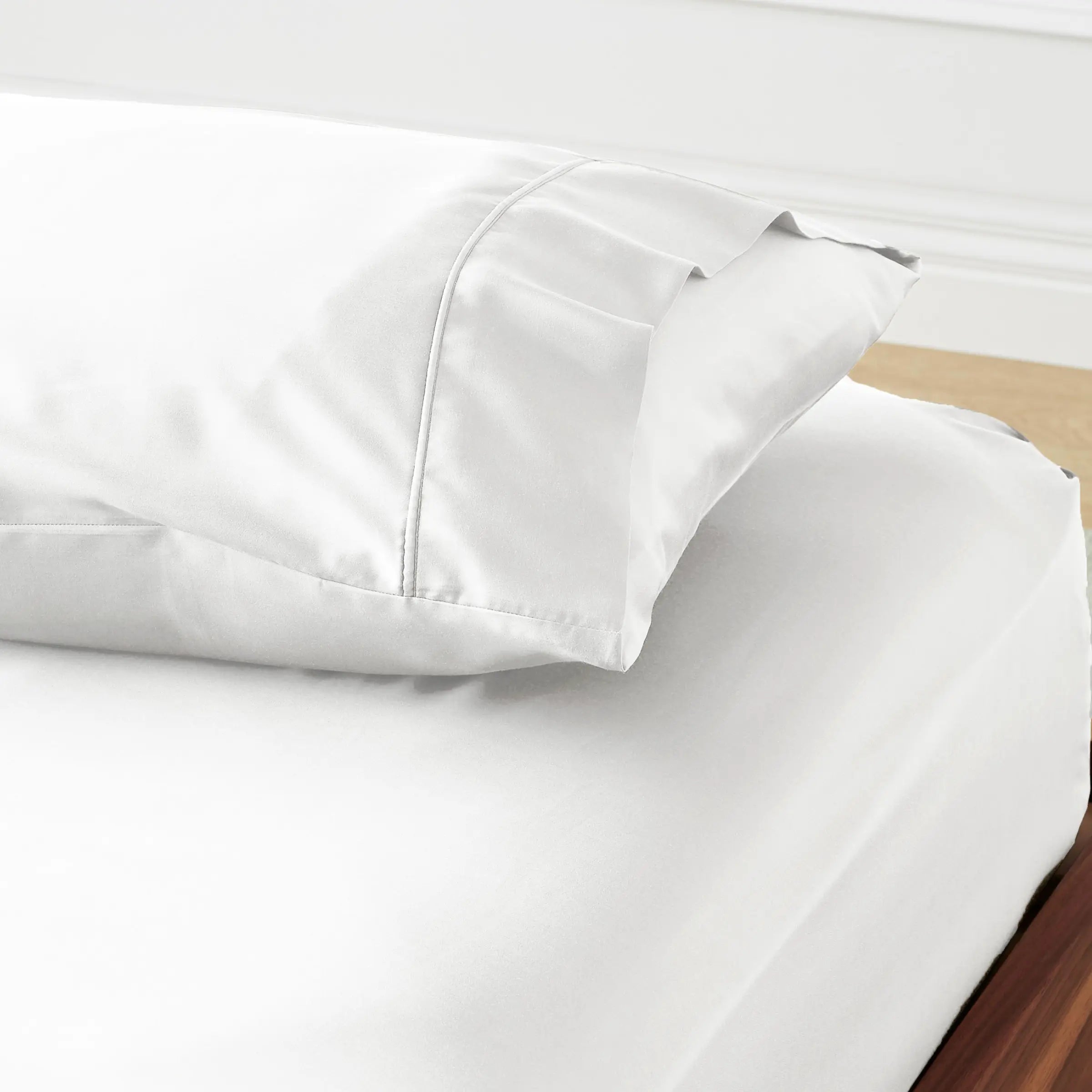 White bed sheets and pillowcase set on a wooden surface