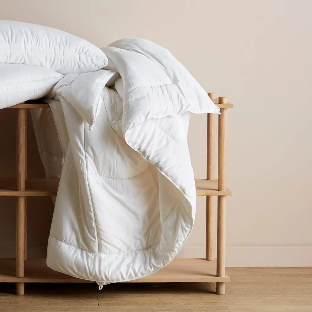 White comforter draped over a wooden bed frame against a beige wall.