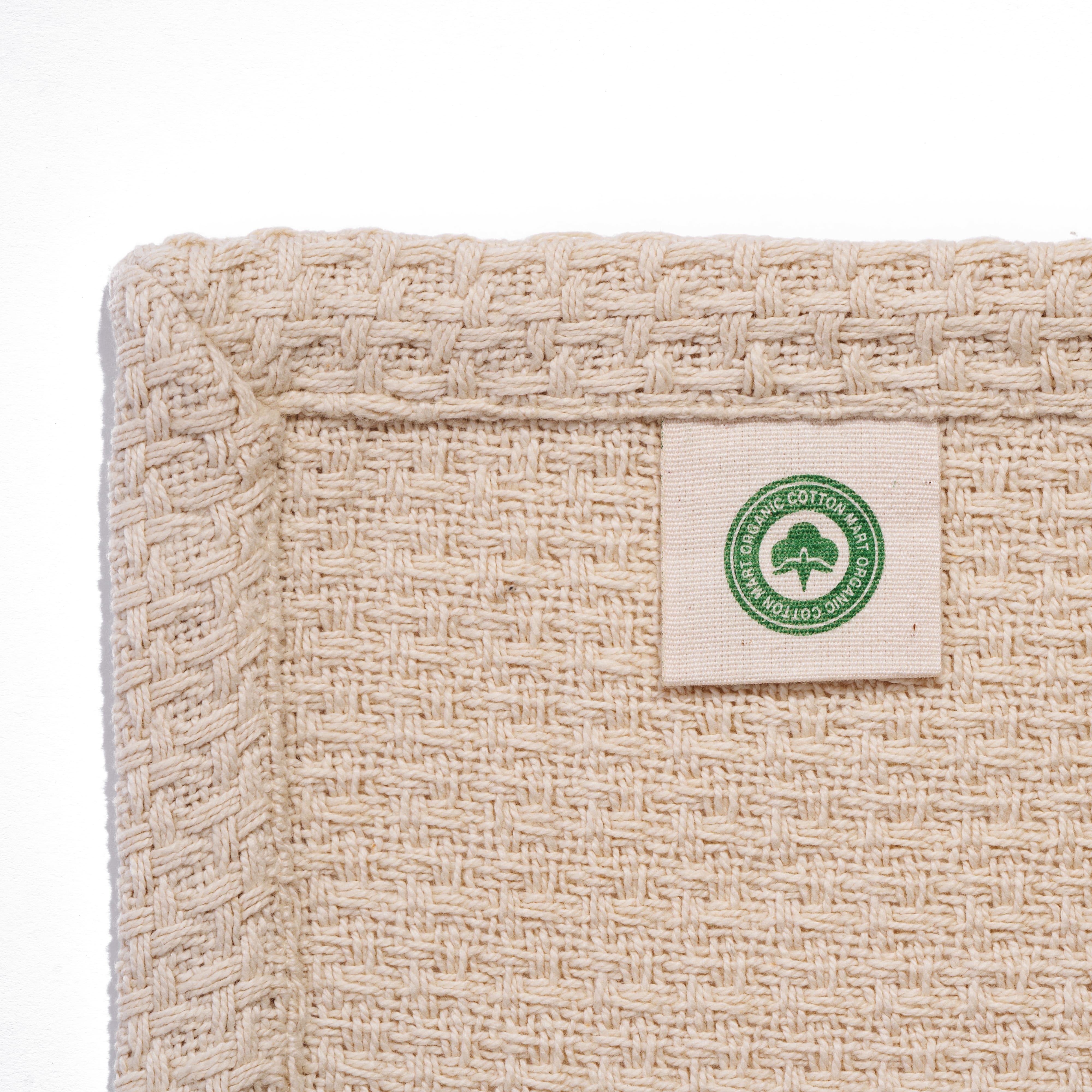 Beige woven fabric with a green organic cotton label on a white background