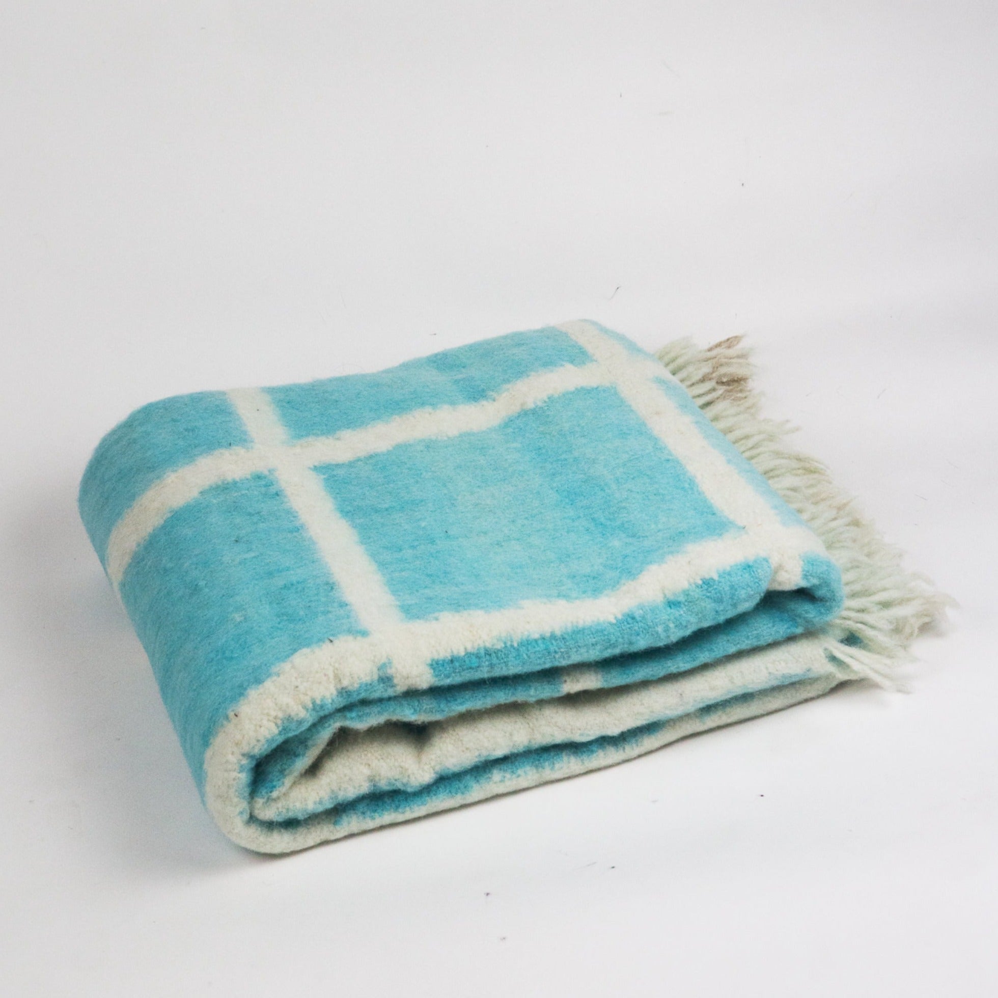 Folded blue and white checkered blanket with fringes on a light gray background