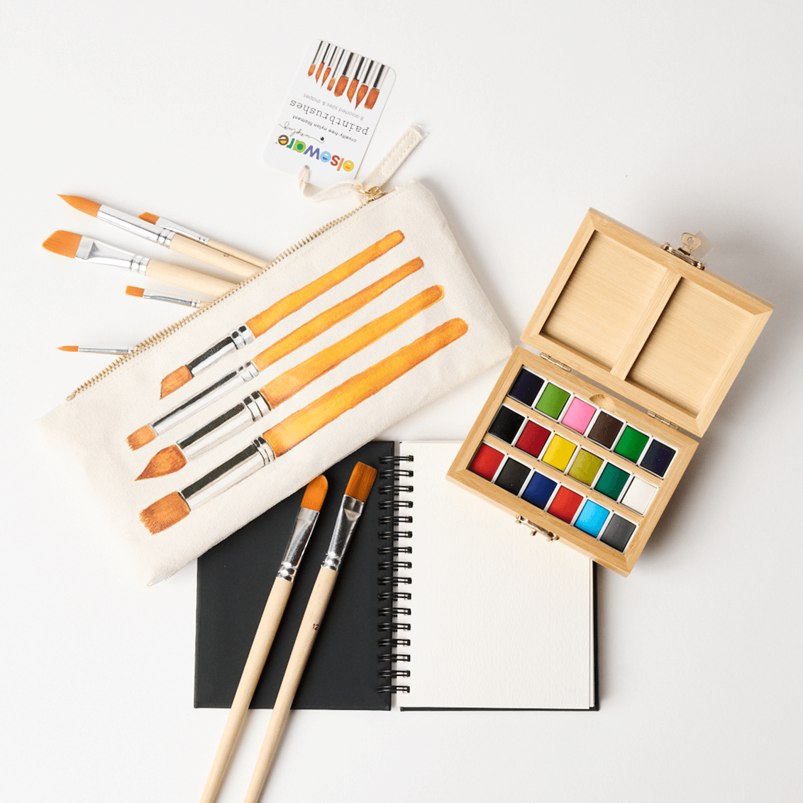 Art supplies including paintbrushes, watercolor paints, and a notebook on a white background
