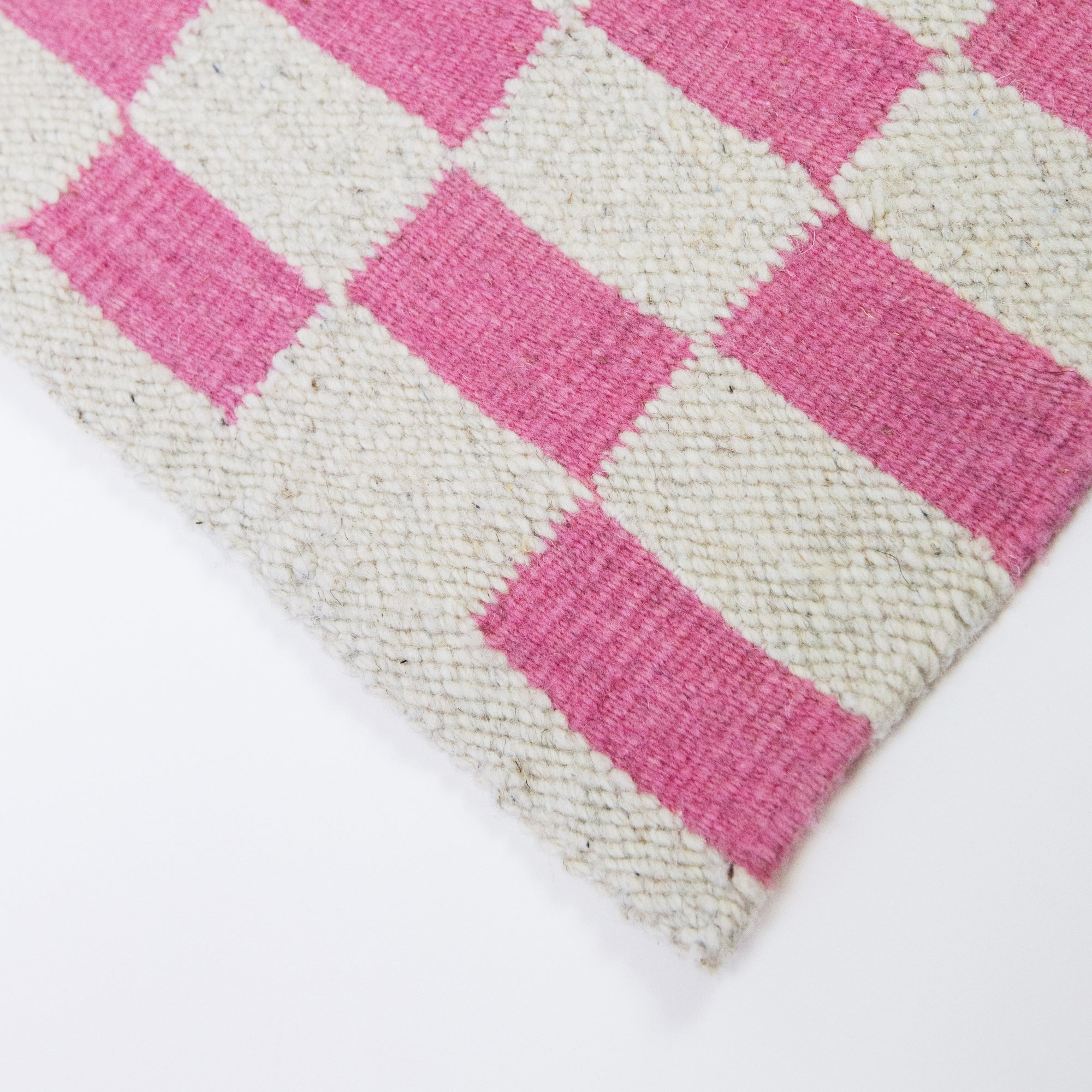 Close-up of a woven mat with pink and beige checkered pattern on a white background