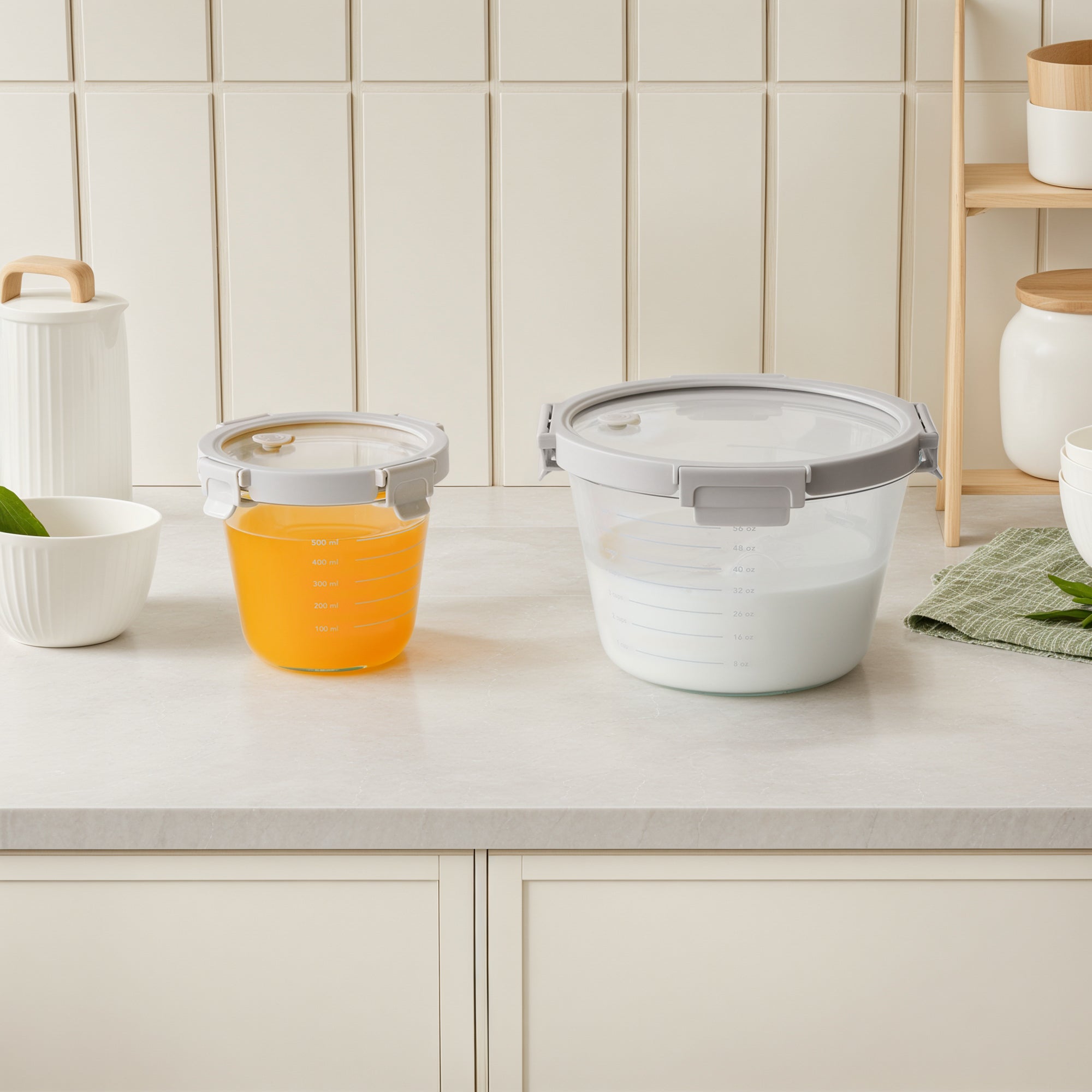 Set of kitchen containers with lids on a countertop against a tiled wall.