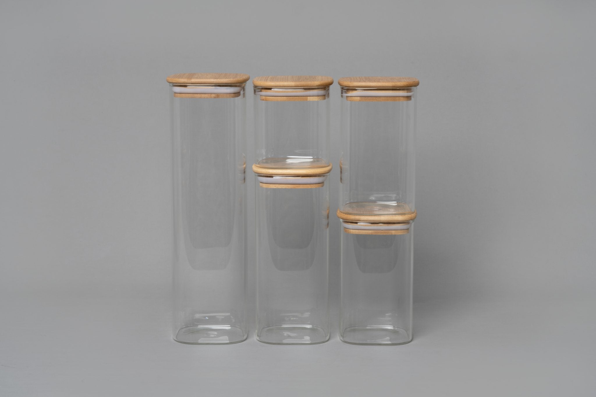 Set of three clear glass jars with wooden lids on a gray background