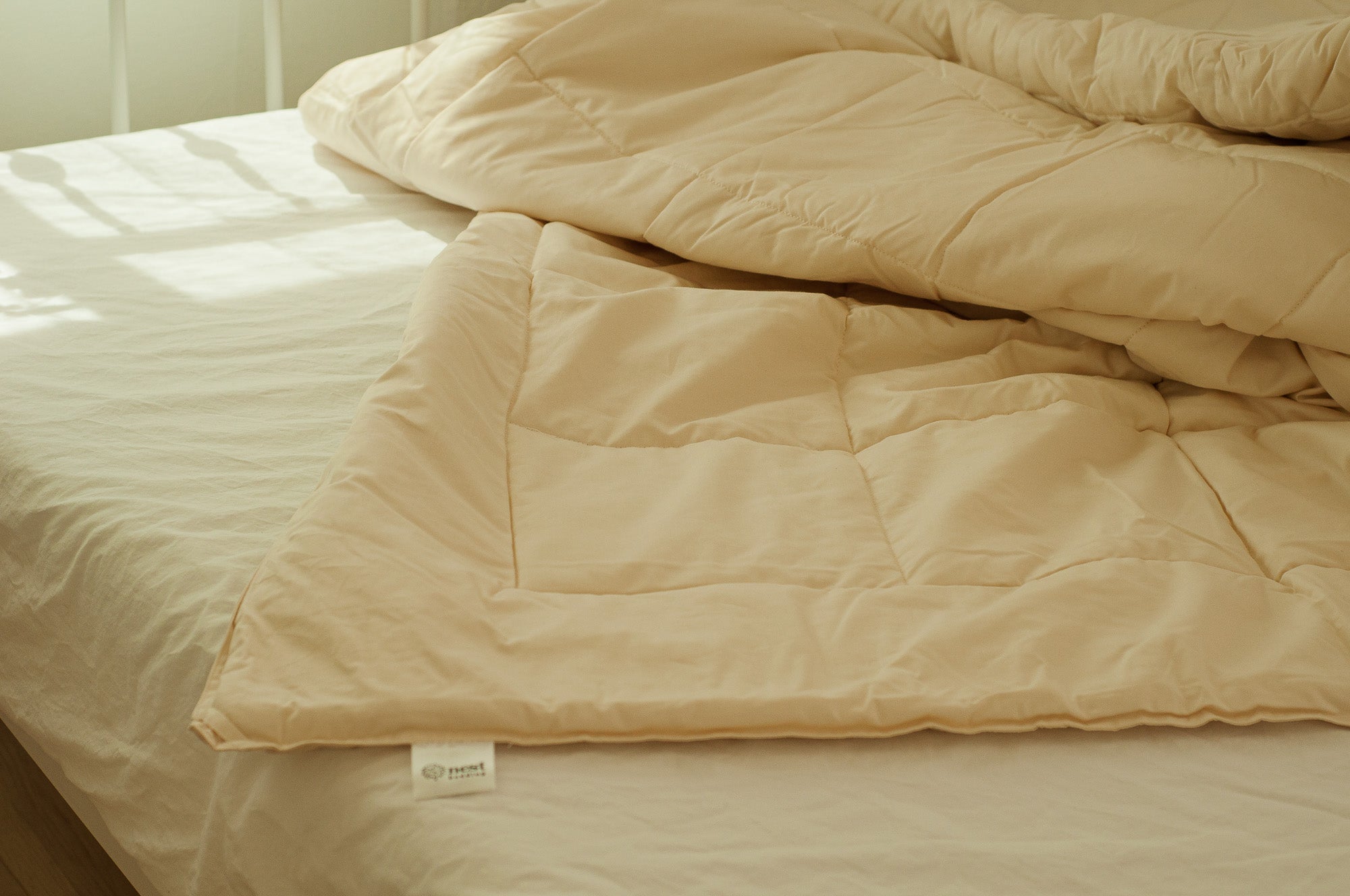 Beige comforter on a bed with a visible brand label.
