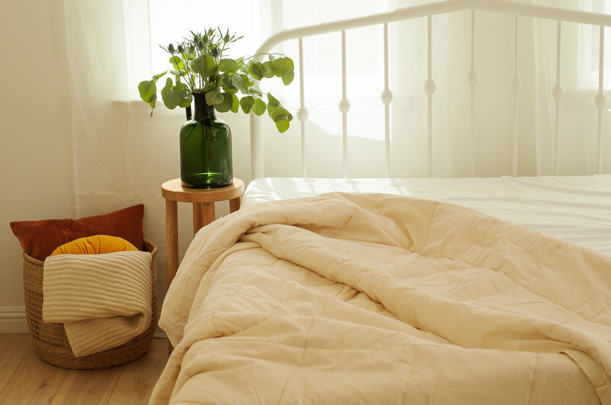 Beige comforter on a bed with a vase of greenery on a side table.