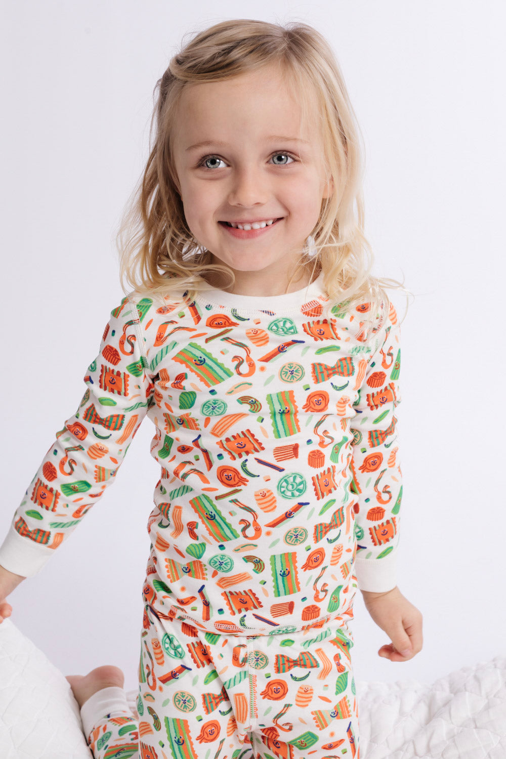 Child wearing a colorful pajama set with a pattern of various items on a white background