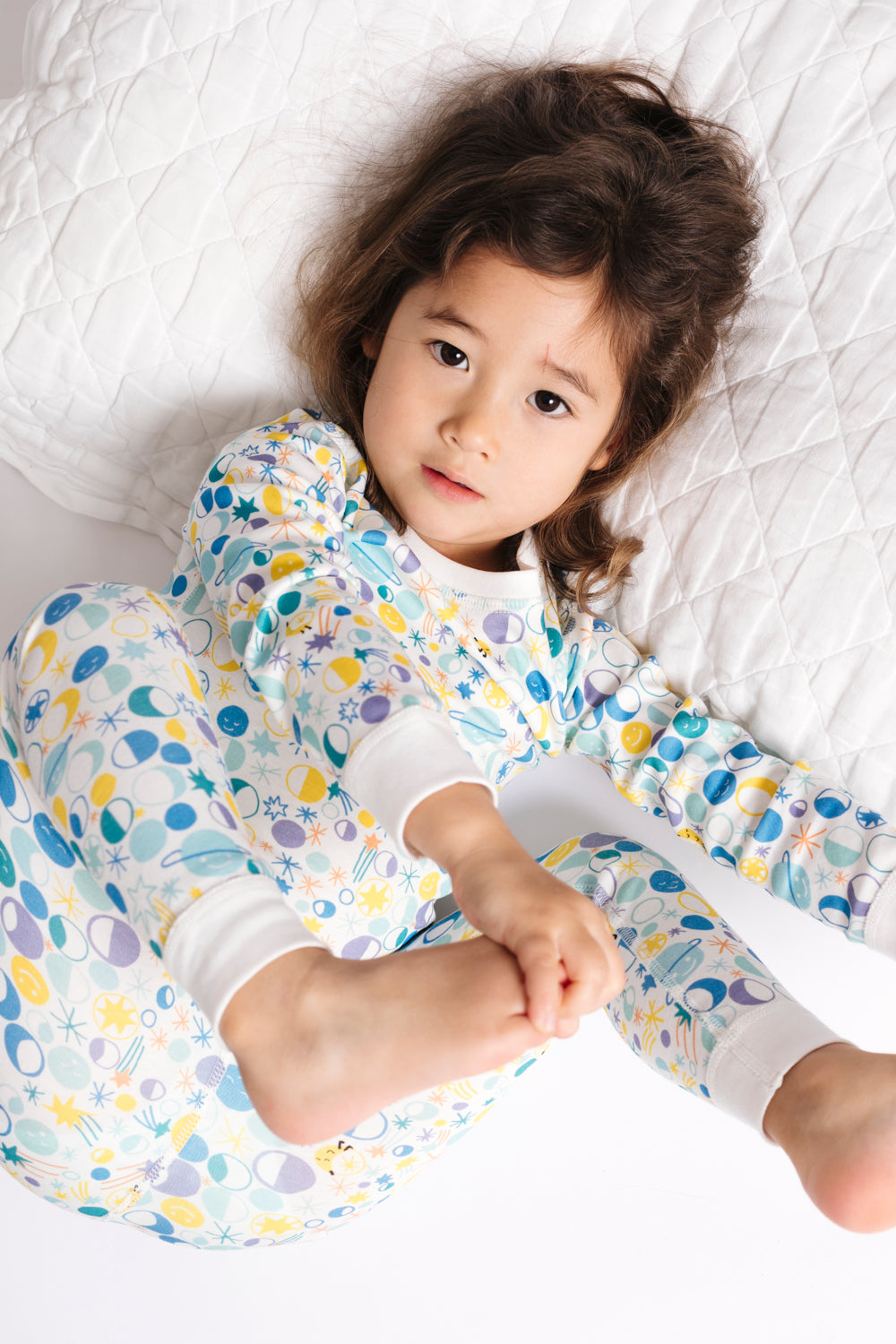 Child wearing colorful pajama pants lying on a white bed