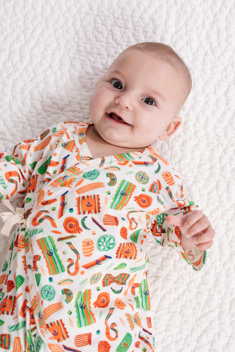 Baby wearing a colorful patterned onesie on a textured white blanket