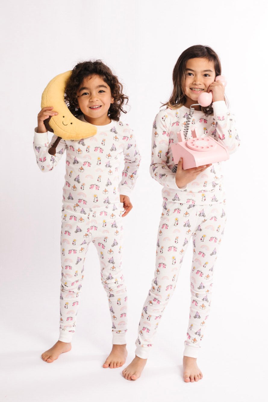 Two children in floral pajamas holding a moon-shaped object and a pink phone on a white background