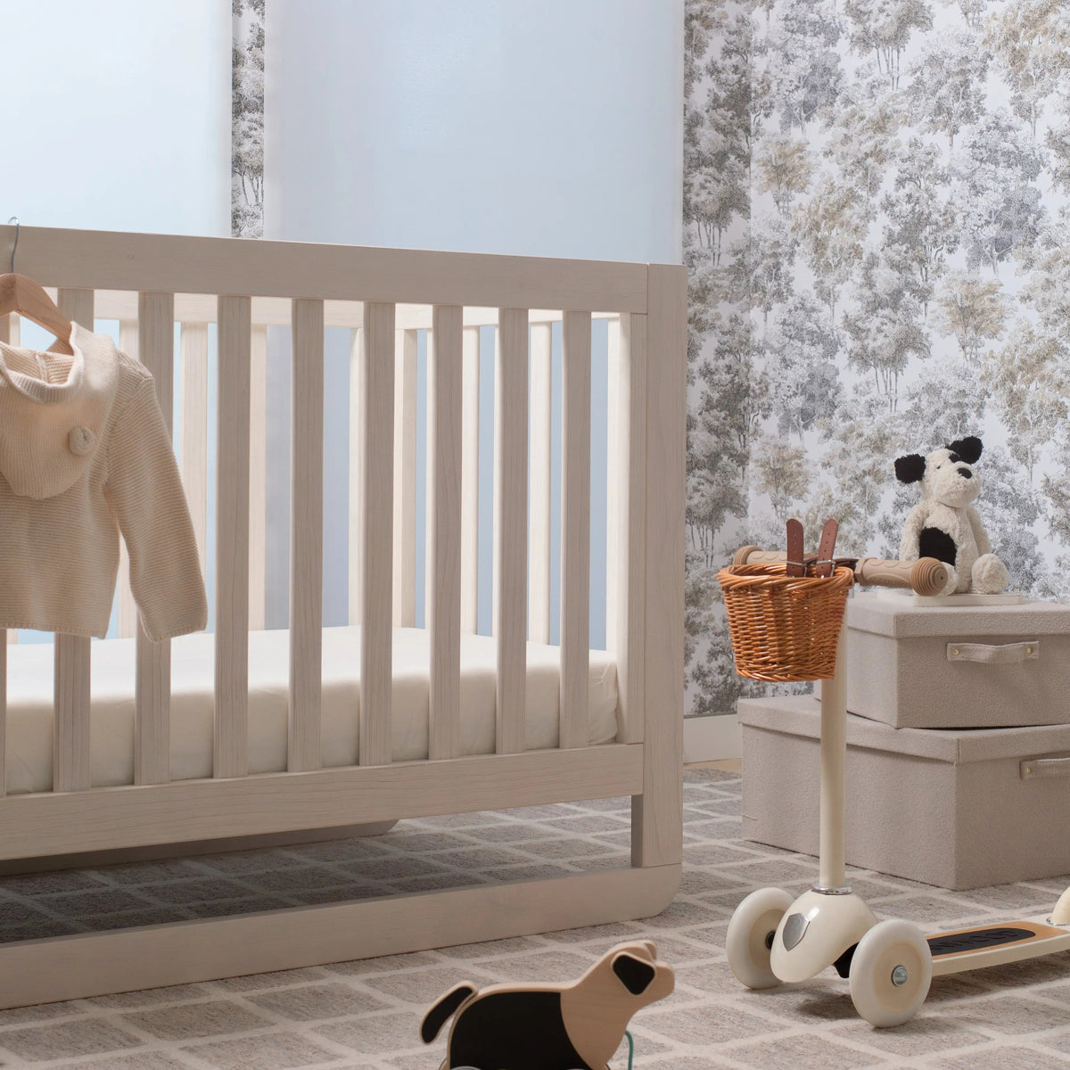 Nursery room with a crib, toys, and a basket against a floral wallpaper wall.