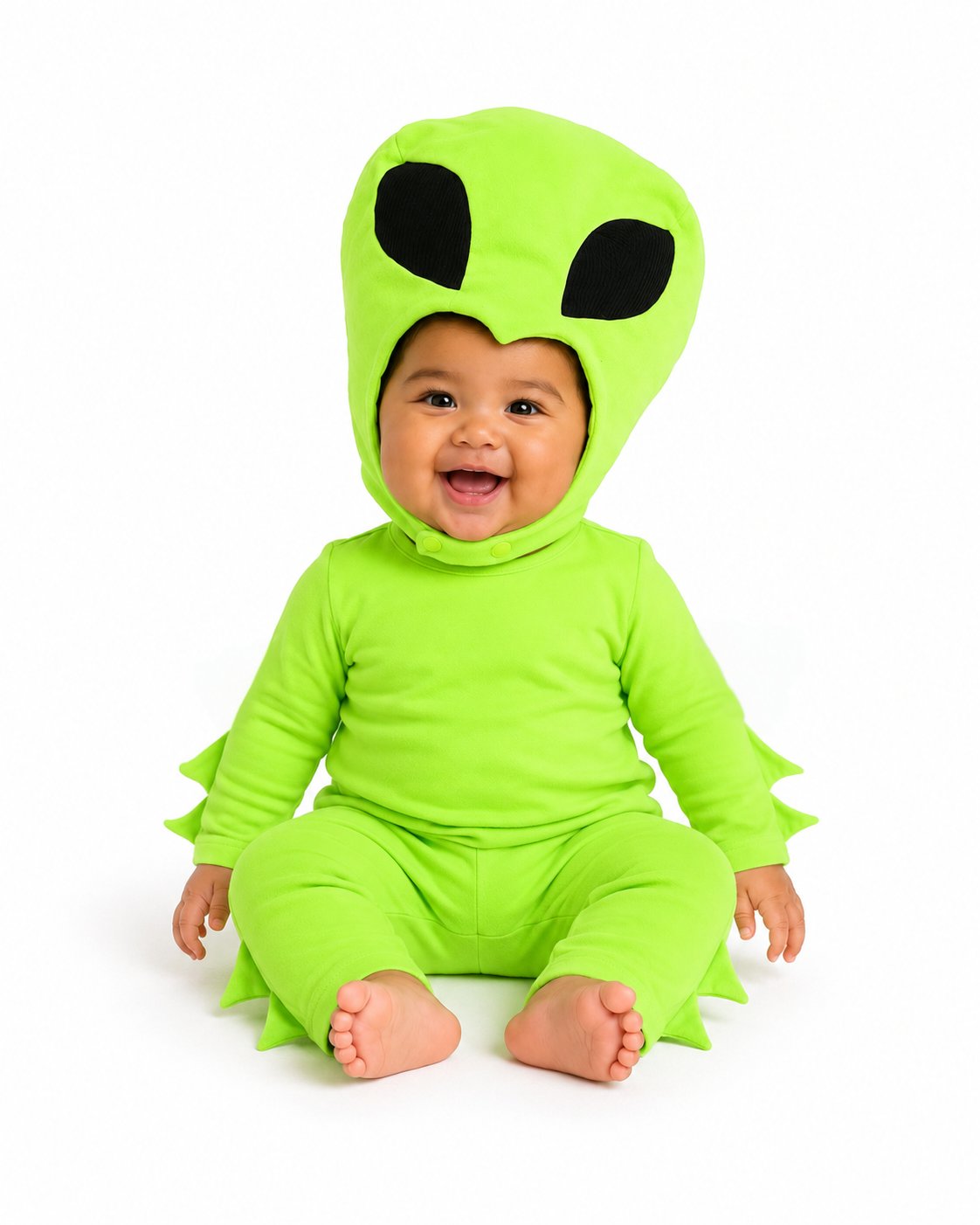 A smiling baby wearing a bright lime green alien costume with a hood featuring large black eyes, seated against a plain white background.