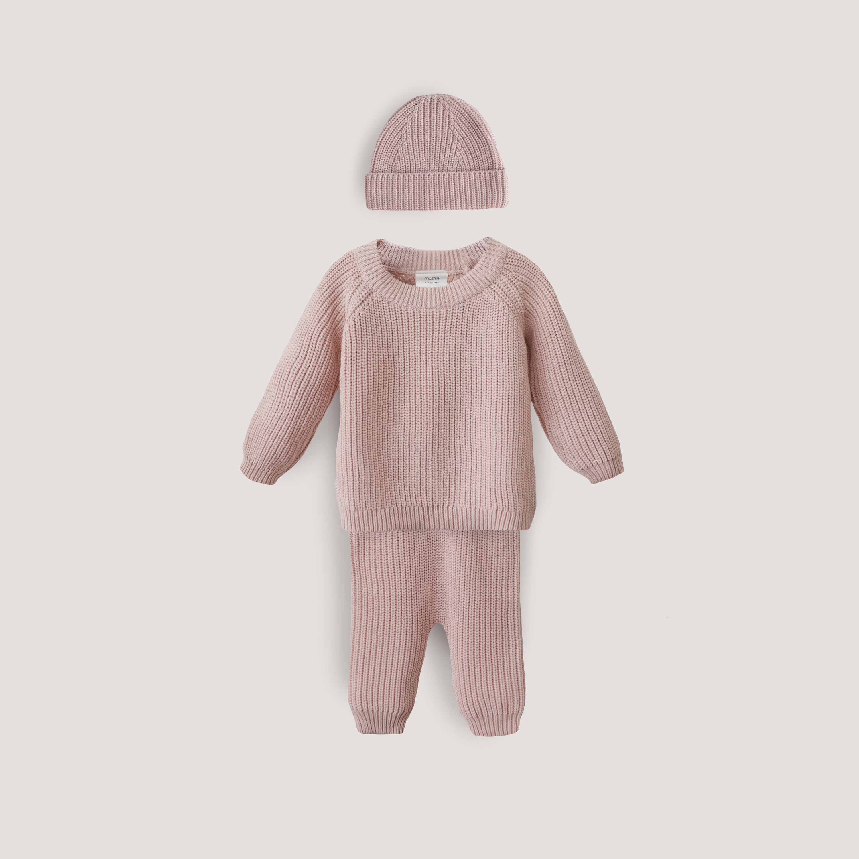 Pink baby outfit with sweater, pants, and hat on a light gray background
