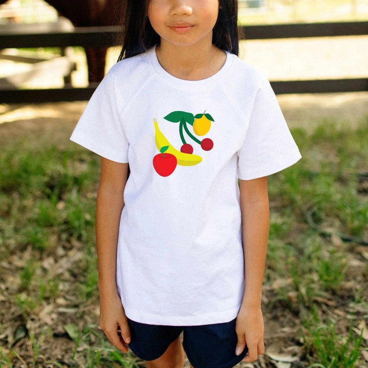 Child wearing a white t-shirt with colorful fruit design outdoors.