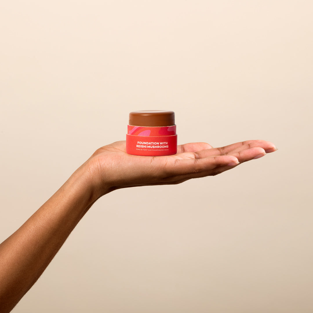 Hand holding a small jar with a beige background