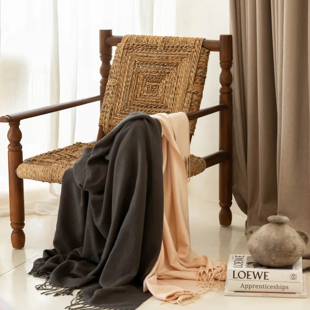 Woven chair with draped scarves and a vase in a softly lit room.