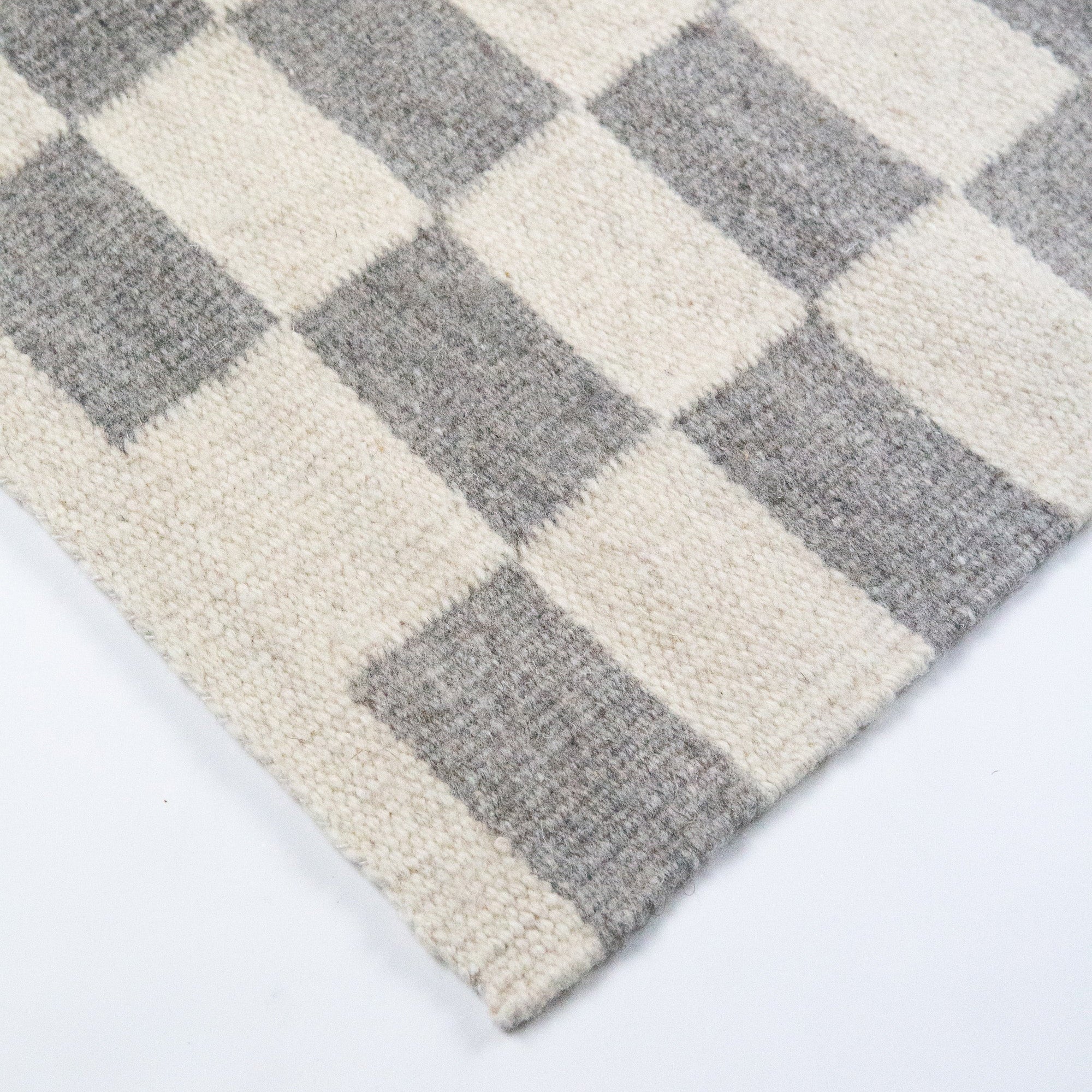 Checkered pattern rug with gray and beige squares on a white background