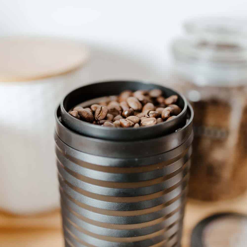 Whole organic coffee beans inside an electric grinder sitting on a countertop in a kitchen.
