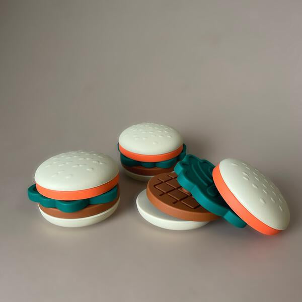 Toy hamburger set with white buns, brown buns, and green and orange slices on a gray background