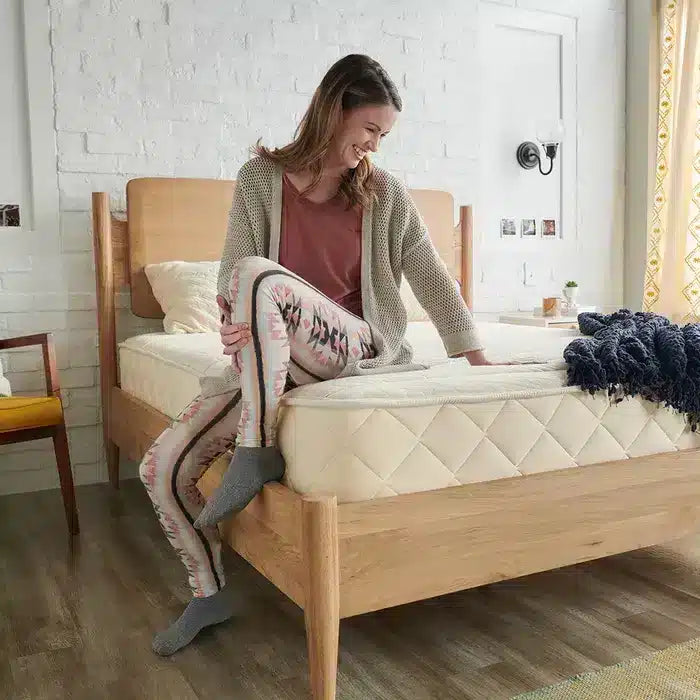 woman sitting on a bed in a room with a white wall and a chair.