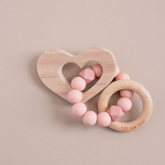 Two wooden baby teething rings with pink beads on a beige background
