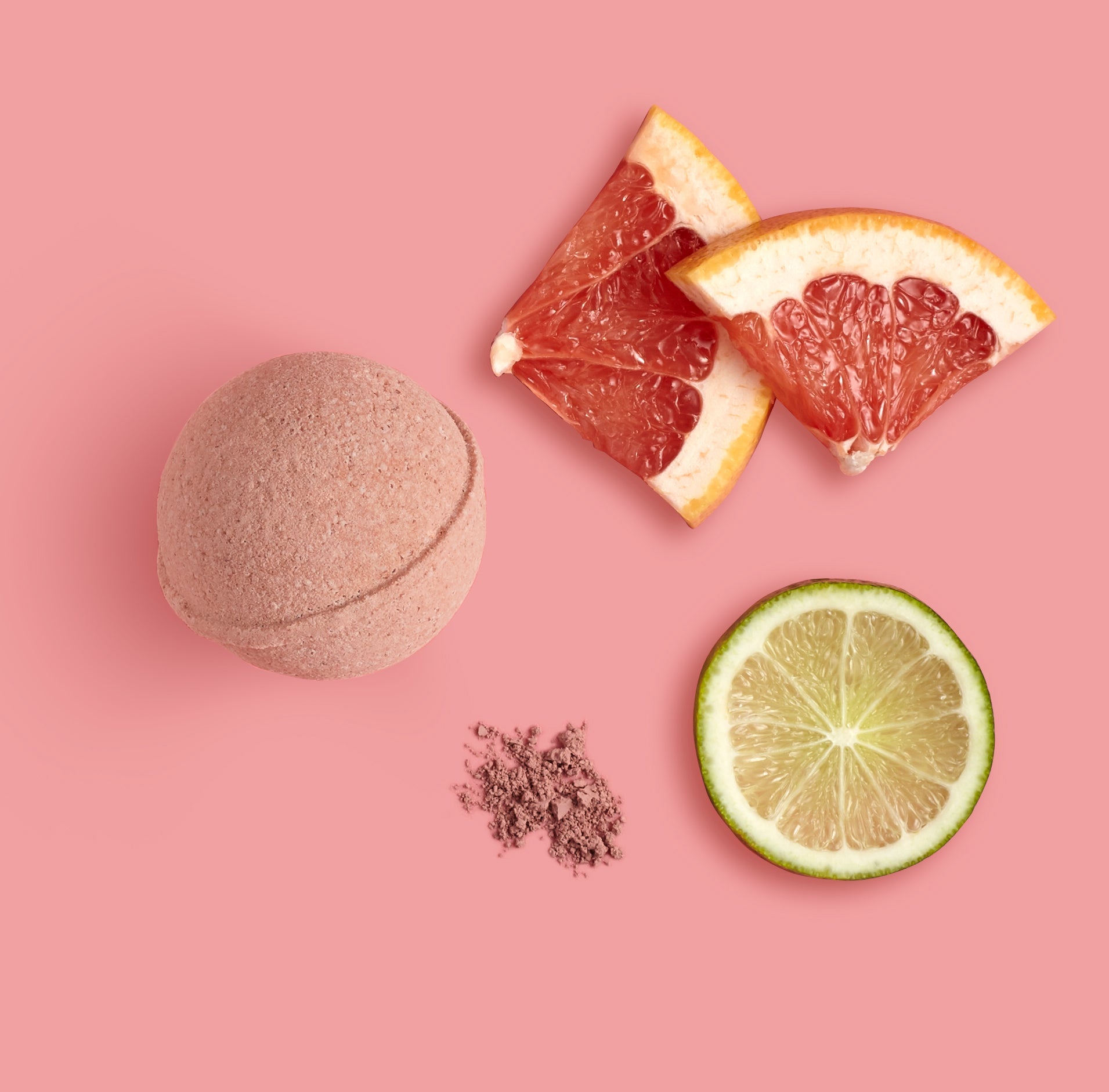 Bath bomb, grapefruit slices, and lime on a pink background