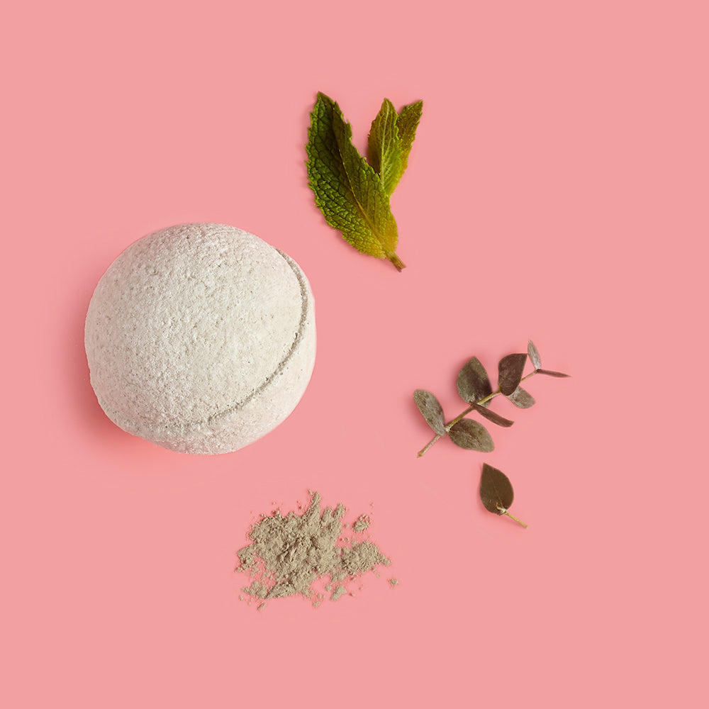 Bath bomb with green leaves and powder on a pink background