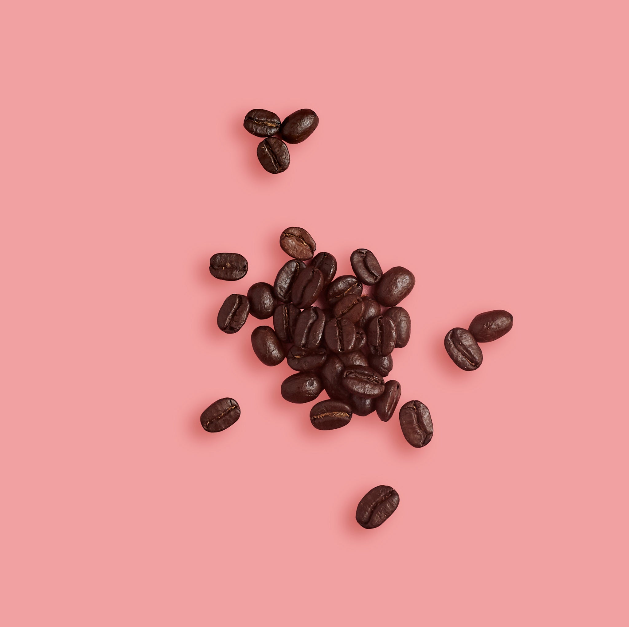 Coffee beans scattered on a pink background