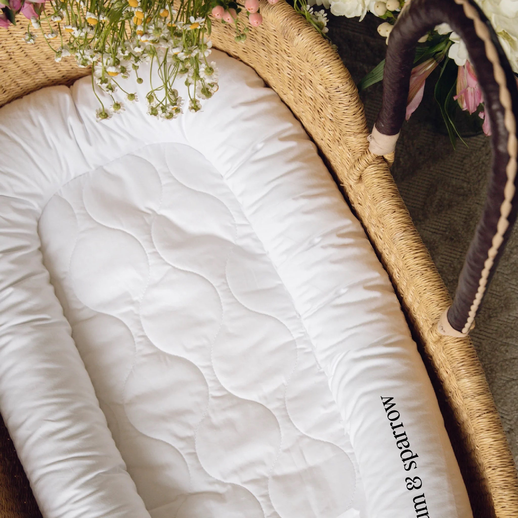 White quilt with 'Plum & Sparrow' branding on a woven basket with flowers.