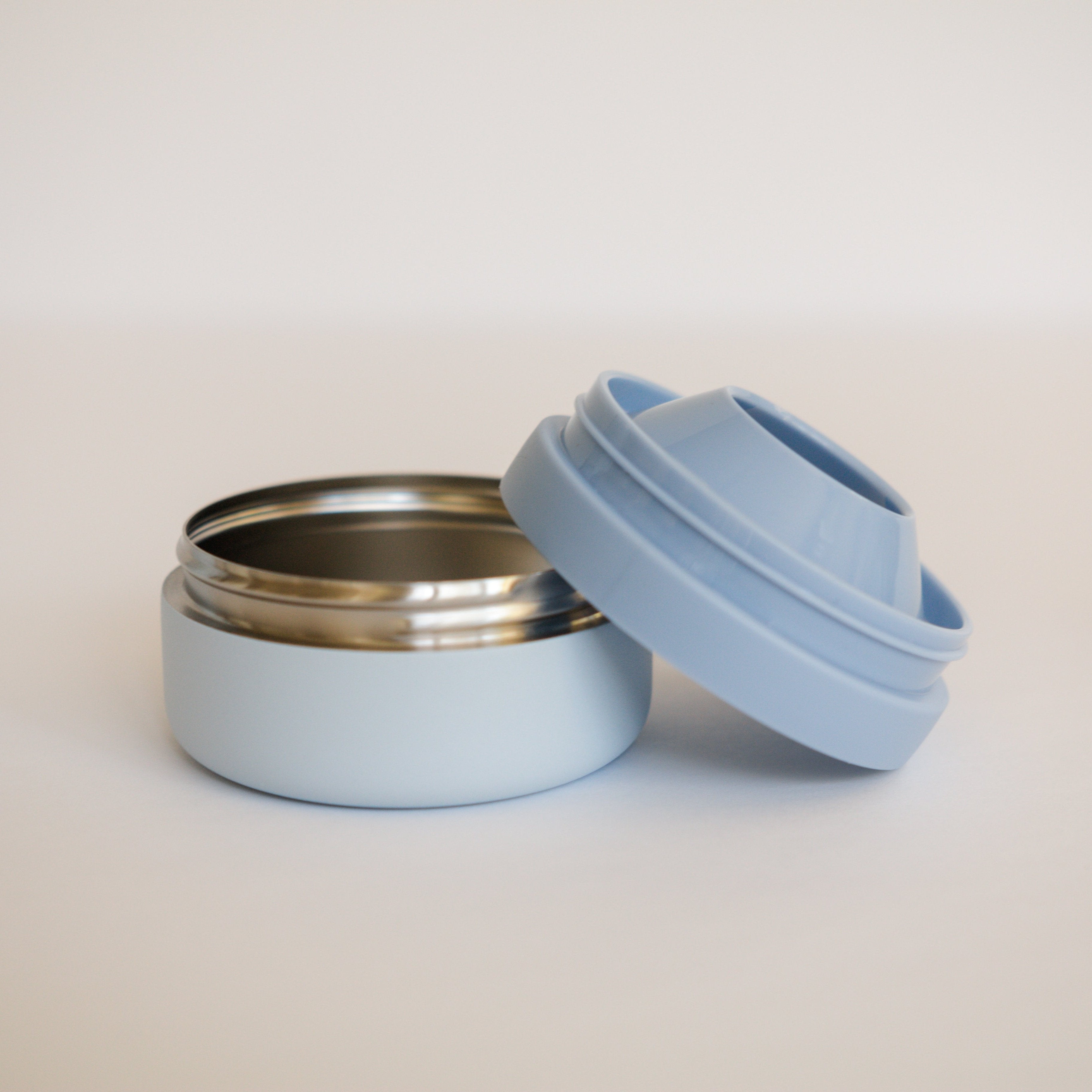 Light blue reusable food container with a silver lid on a beige background