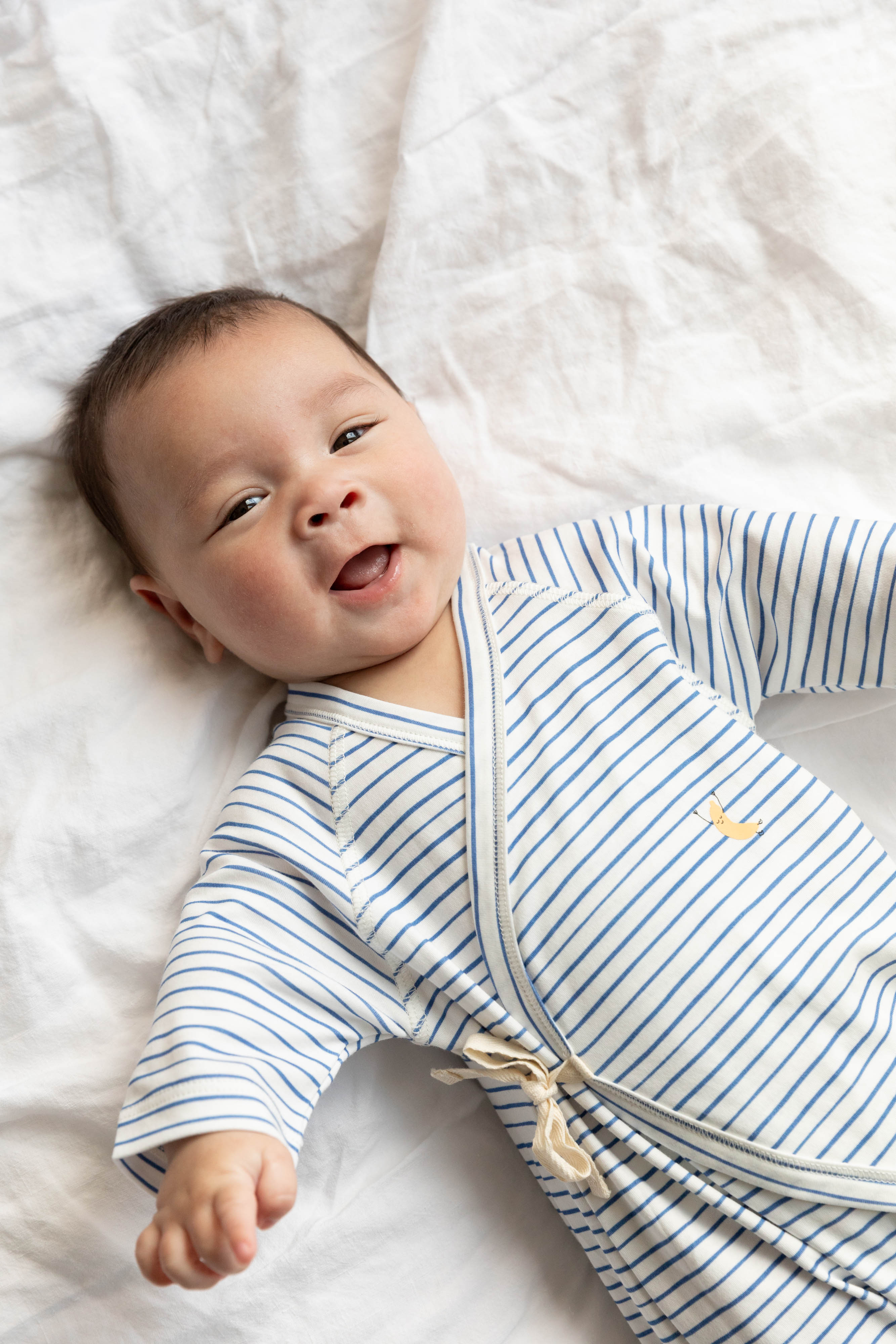 Baby wearing a blue and white striped onesie lying on a white blanket