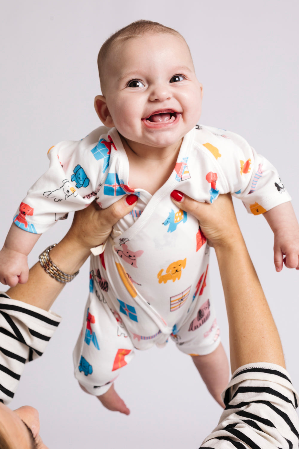 Baby in a colorful onesie being held by an adult against a plain background